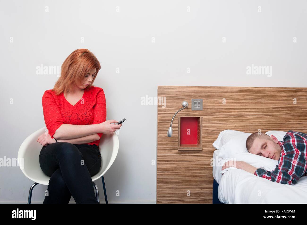 Junge Frau mit Handy, während Ihr Partner schläft Stockfoto