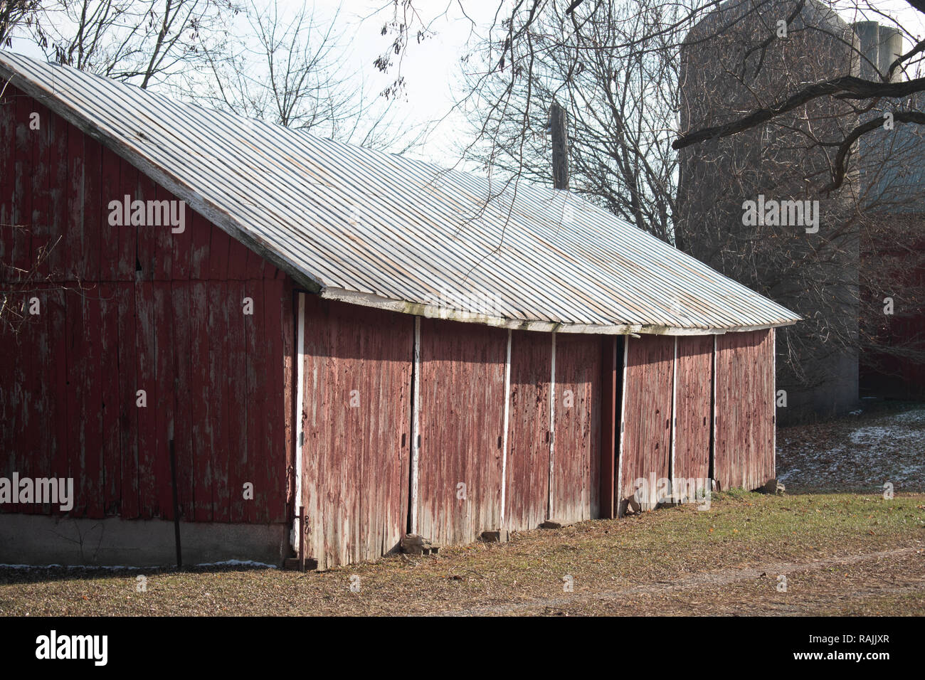 Alte rot Bauernhof Schuppen oder Stall mit Silos im Hintergrund, im späten Herbst Stockfoto