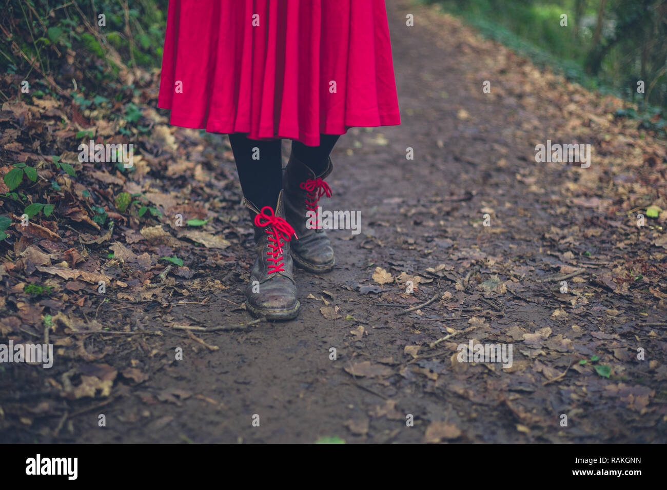 Eine Frau trägt Stiefel und ein Kleid ist zu Fuß auf einem Pfad in den Wald Stockfoto