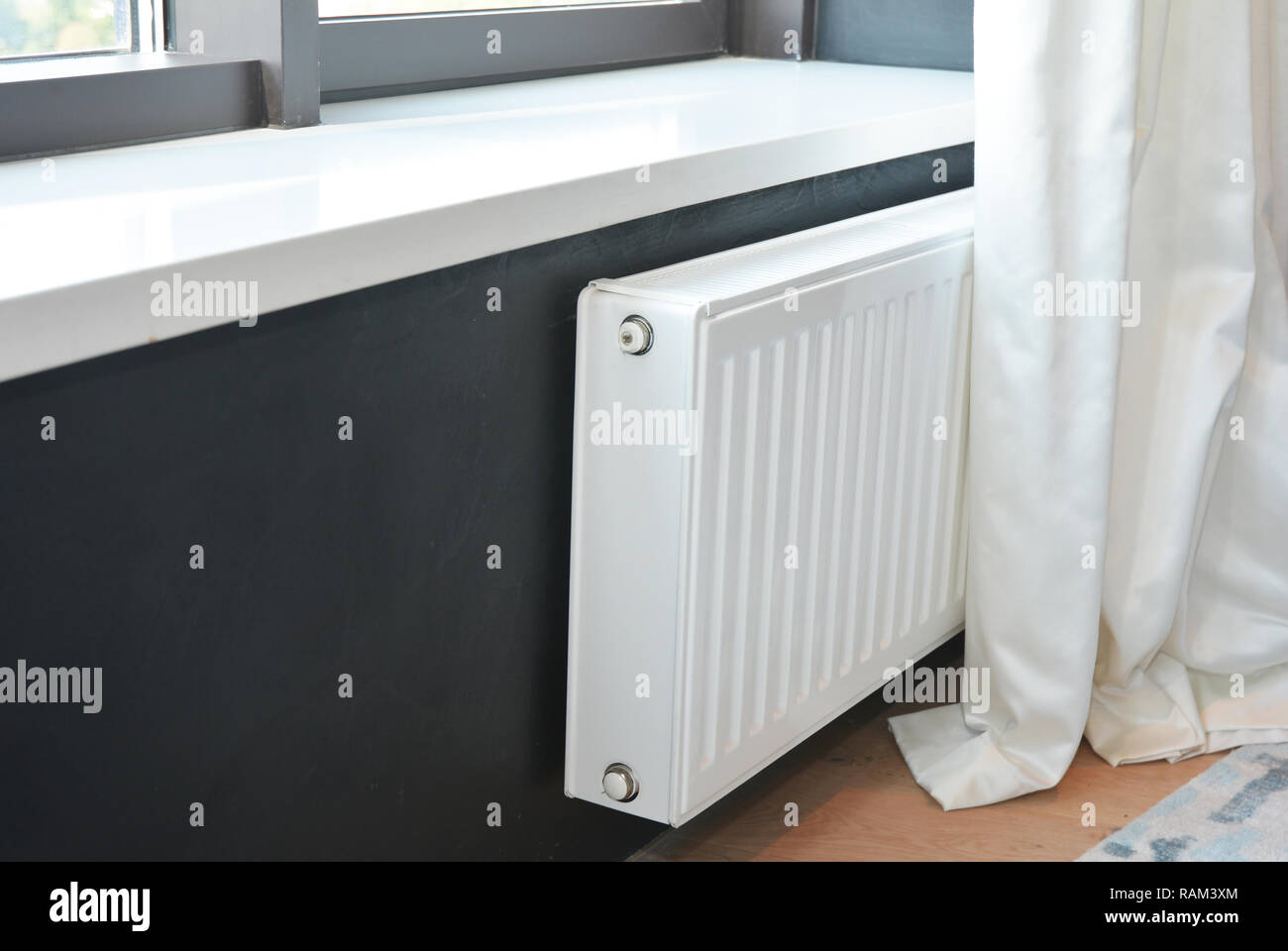 Weiße Heizkörper Heizung mit Thermostat zur Energieeinsparung im luxuriösen Schlafzimmer mit schwarzen Wänden und whitesun blind. Stockfoto