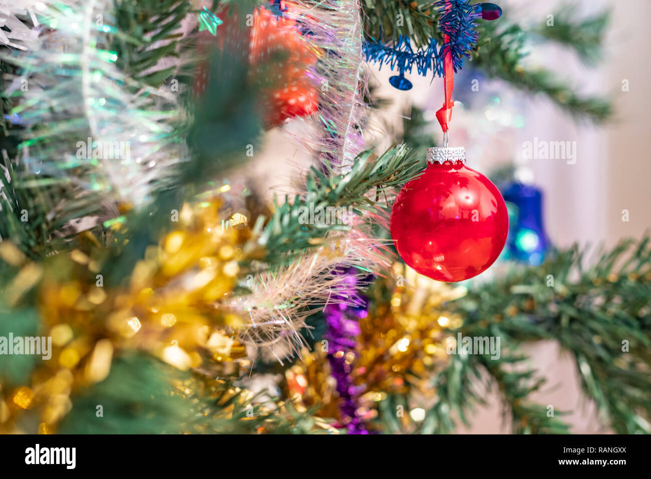 Nahaufnahme von einem roten Weihnachtsdekoration christbaumkugel Übergabe von einem Xmas Tree Branch. Verschwommen und defokussiertem Hintergrund und Vordergrund. Stockfoto