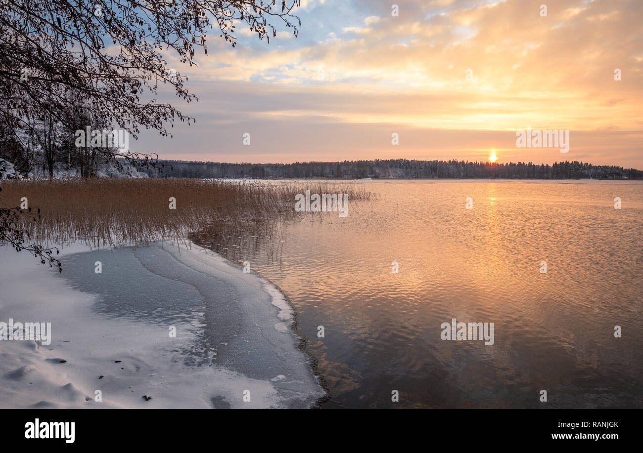 Malerische Winterlandschaft mit Sonnenuntergang am eisigen und friedlichen See in Finnland Stockfoto