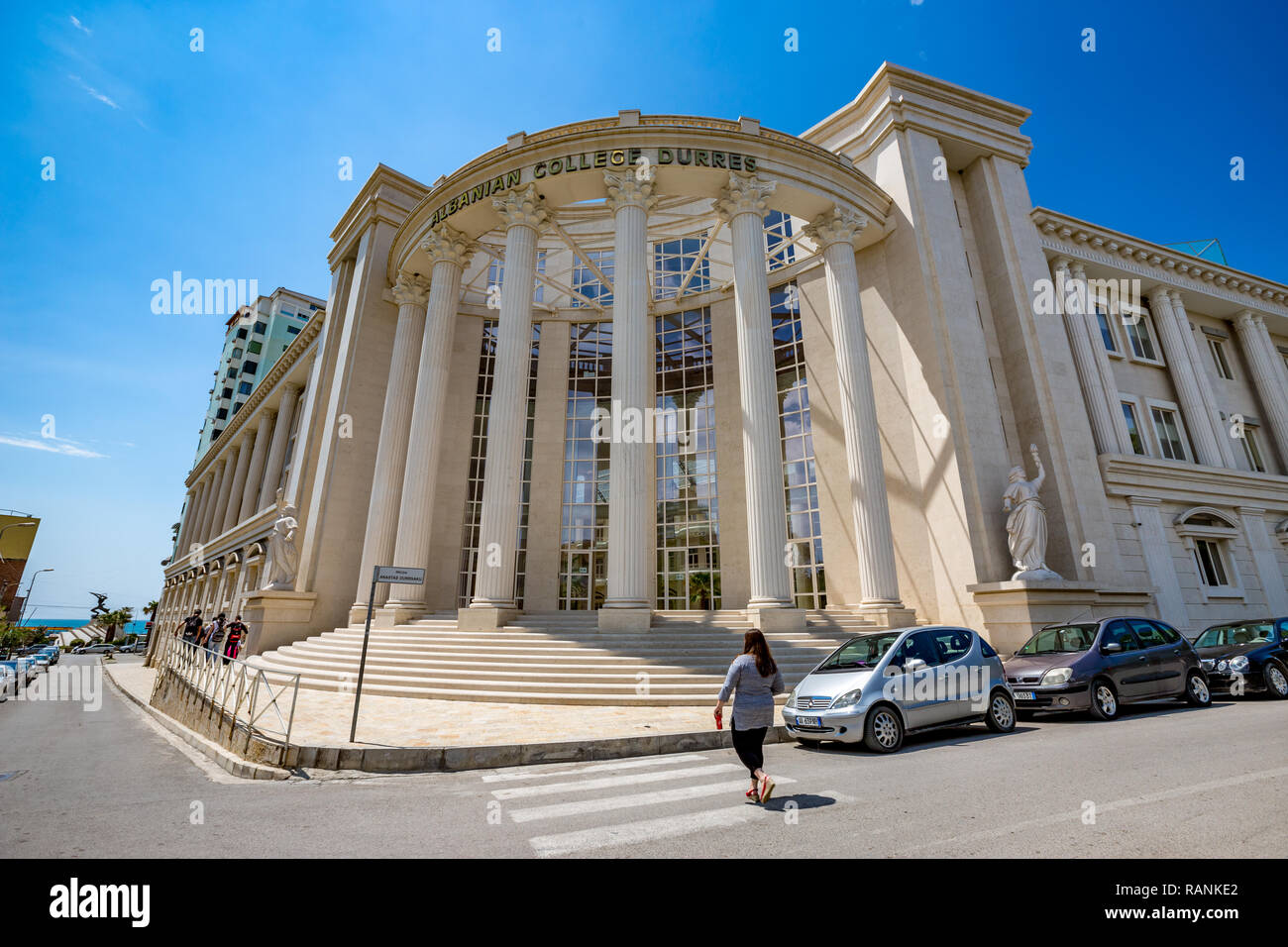 DURRES, Albanien - 17. MAI 2017: Frau auf dem Gehweg, Zebrastreifen vor der albanischen College von Durres. Atemberaubende Architektur mit hohen c Stockfoto