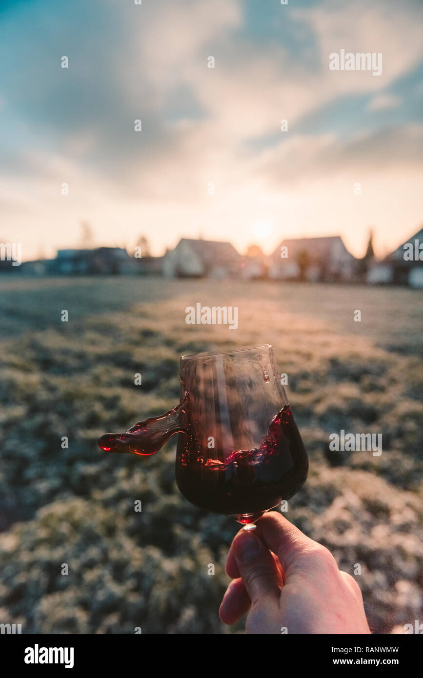Point-of-View-Shot aus einer Hand mit einem Glas Rotwein in die Sonne Stockfoto