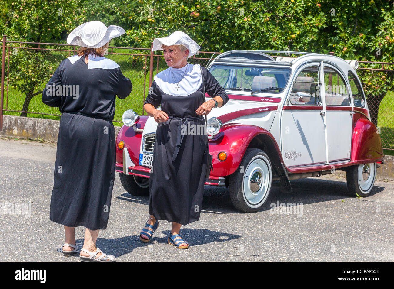 Zwei Frauen in Nonnenkostümen, ein Veteranenauto Citroën 2CV, spezielle zweifarbige Charleston-Version (Kombination aus burgunderrotem Delage Red und weiß-Grau) Stockfoto
