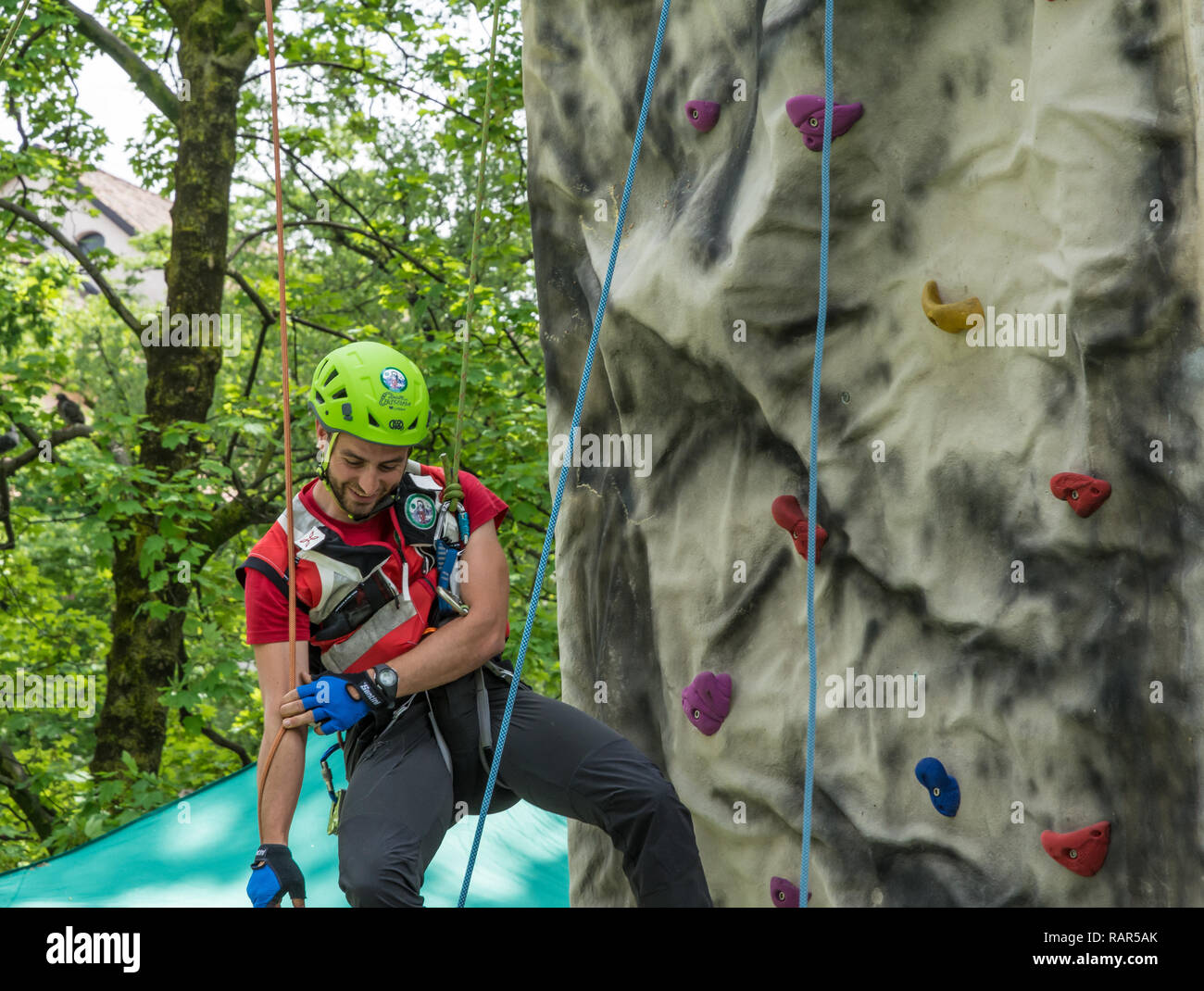 Männliche Lehrer Unterstützung ein schuljunge künstlichen Mauer zu klettern Stockfoto