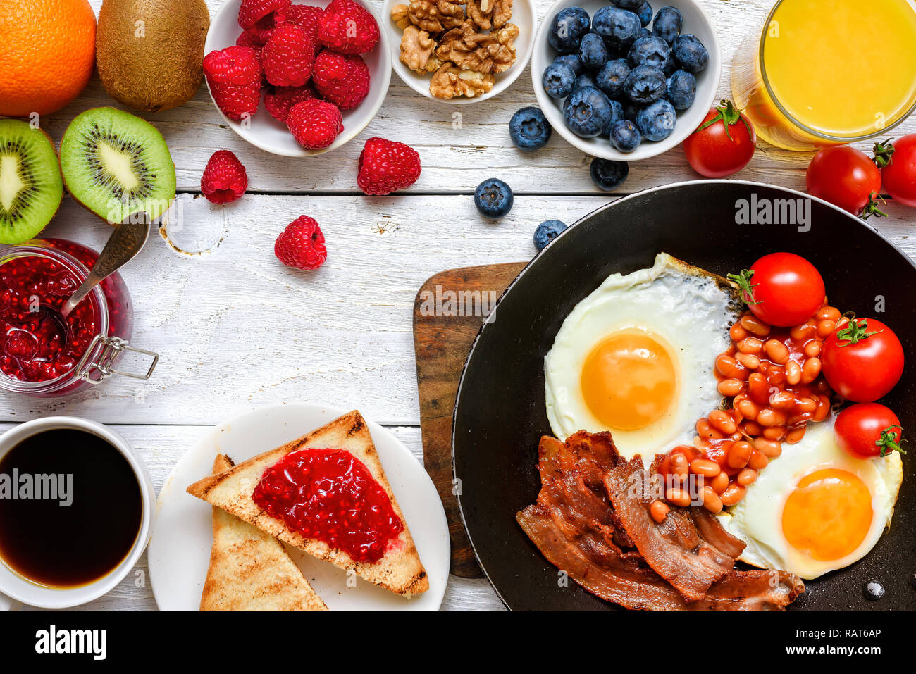 Englisches Frühstück - Spiegeleier, Bohnen, Tomaten, Kaffee, Speck und Toast mit Orangensaft, frisches Obst und Beeren. Ansicht von oben Stockfoto