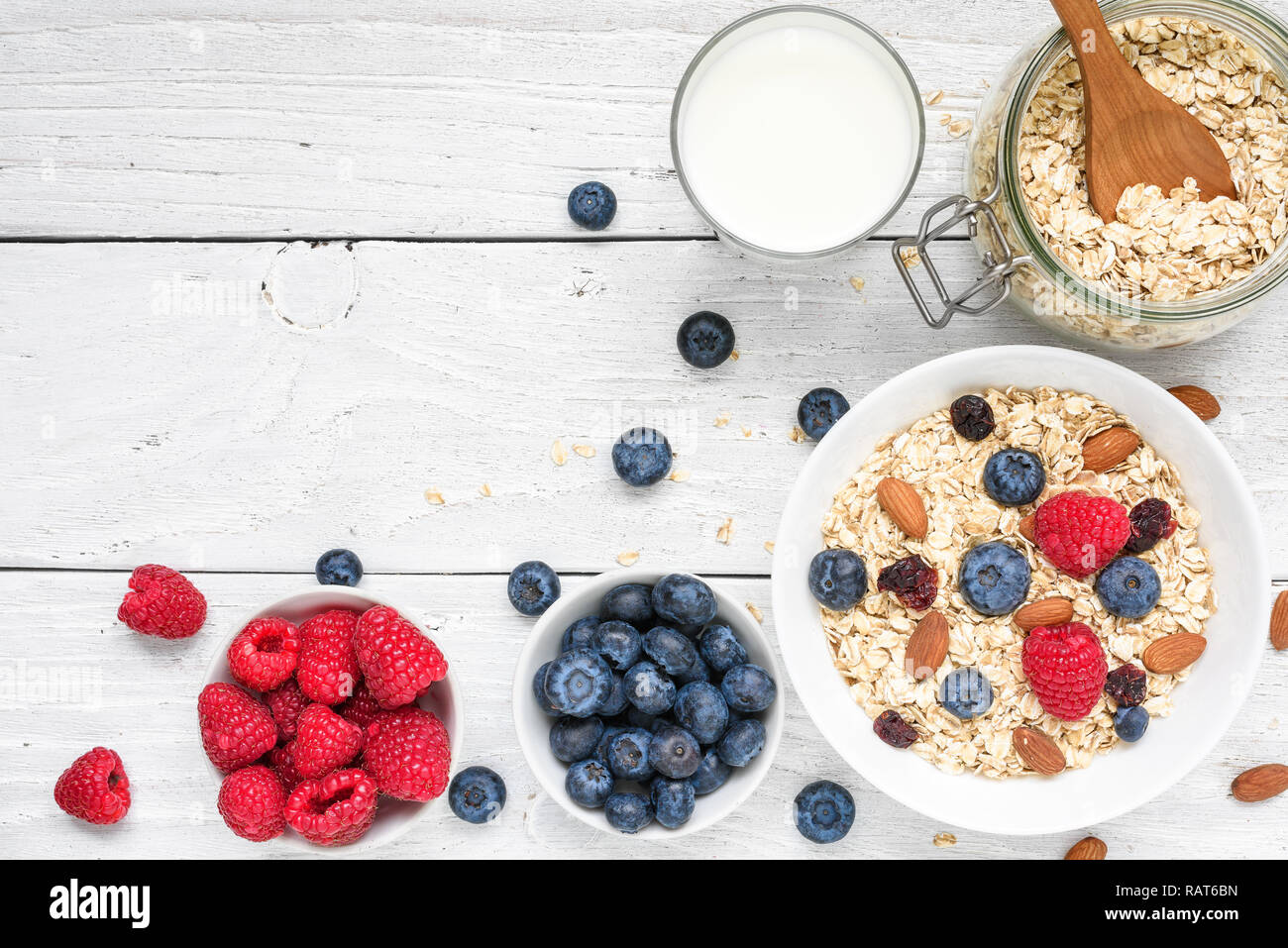 Gesundes Frühstück Zutaten. hausgemachte Hafer mit Himbeeren und Blaubeeren, Milch und Nüssen auf weißem Holz- Hintergrund. Ansicht von oben mit der Kopie Raum Stockfoto