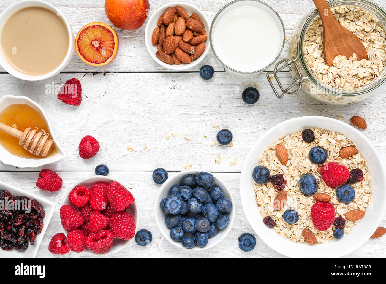 Essen Rahmen aus Frühstück Zutat. Müsli, Früchte, Beeren, Cappuccino, nony, Milch und Muttern auf weiße Holztisch. gesundes Essen. Ansicht von oben mit c Stockfoto