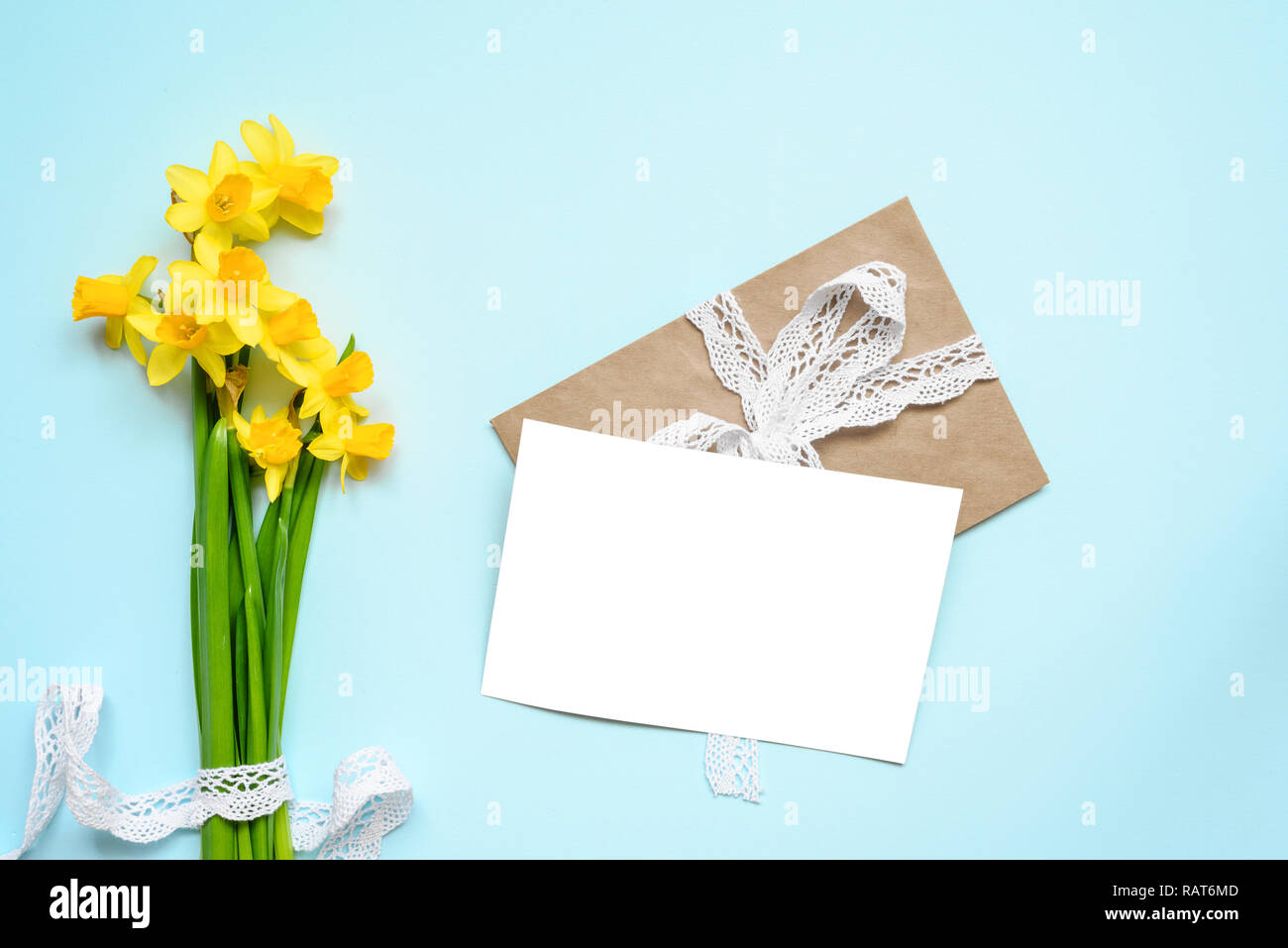 Leere weiße Grußkarte mit Frühling gelb Narcissus Blumen Blumenstrauß über blauen Hintergrund. Mock up. top View Stockfoto