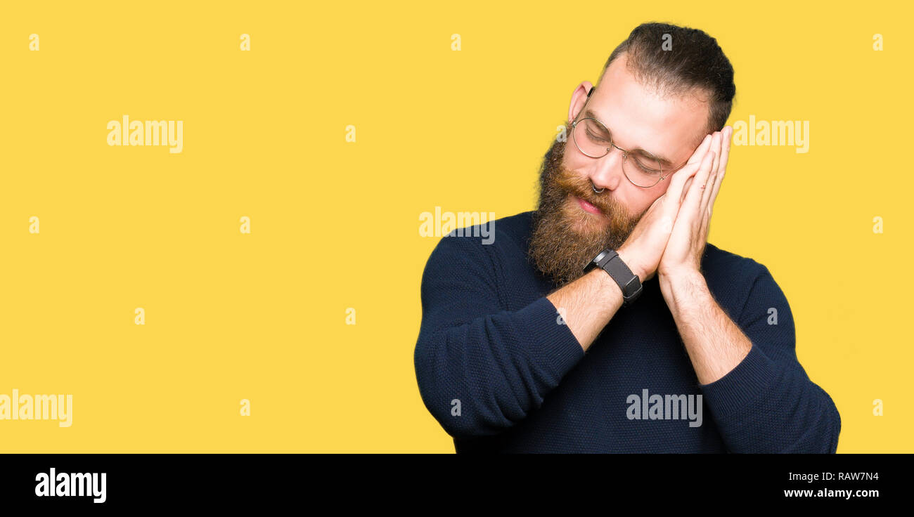 Junge blonde Mann mit Brille und rollkragen pullover müde schlafen, träumen und mit den Händen zusammen posieren während lächelnd mit geschlossenen Augen. Stockfoto