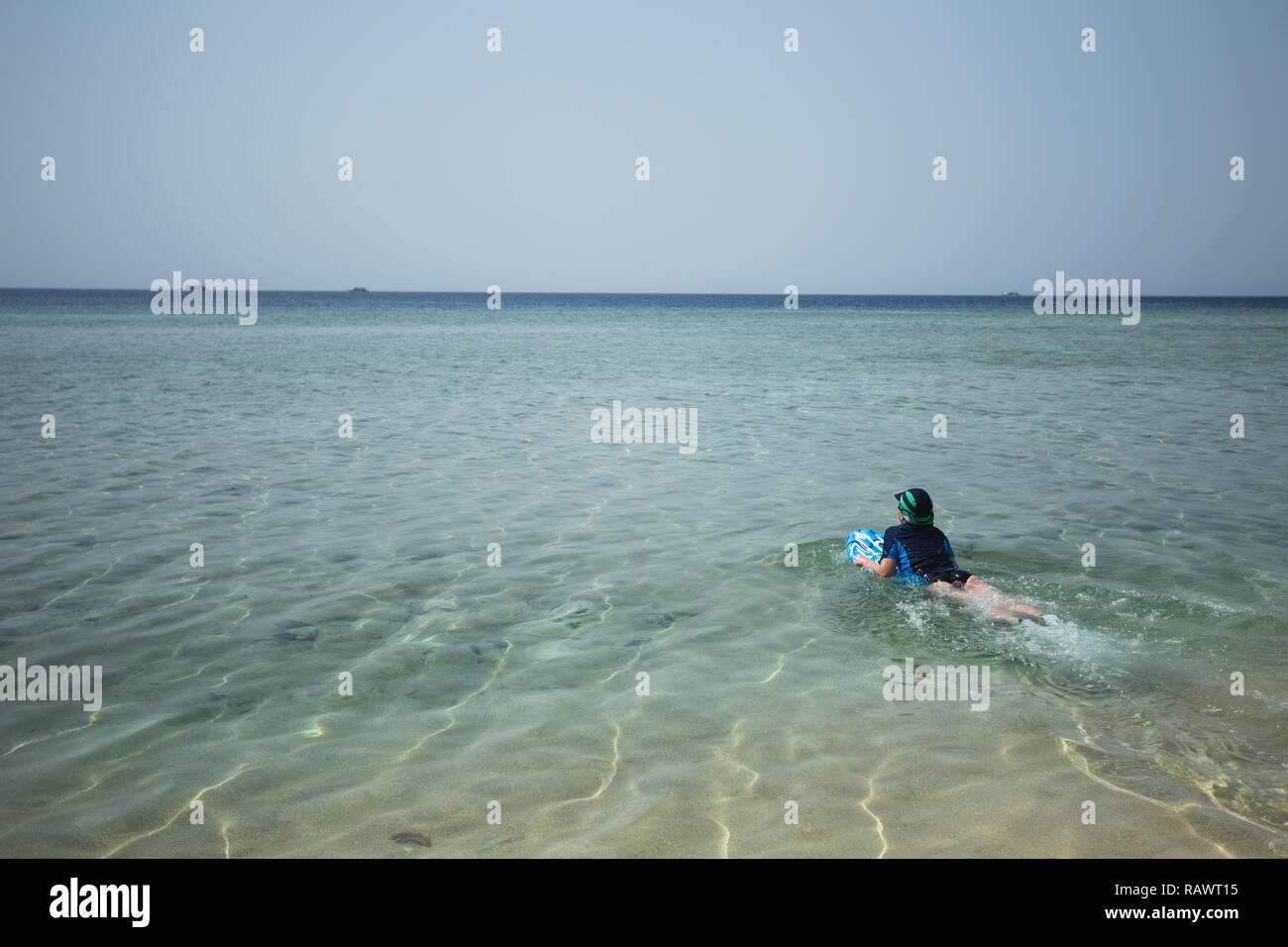 Süße weiß gegerbt Kid im Badeanzug, Kappe und Aqua schuhe Spaß am Sommer, der Sandstrand mit Blau aufblasbares Surfboard gekleidet. Horizontale Farbe phot Stockfoto