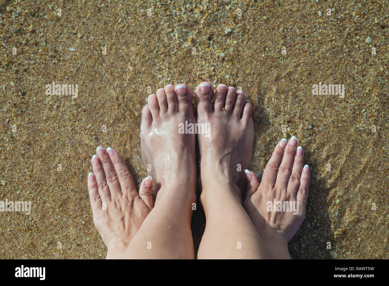 Closeup Top View Photo weiblicher Füße und Hände mit frischem französischen rosa und weißen Pediküre und Maniküre. Frau entspannen im Sommer Sandstrand sitzen o Stockfoto