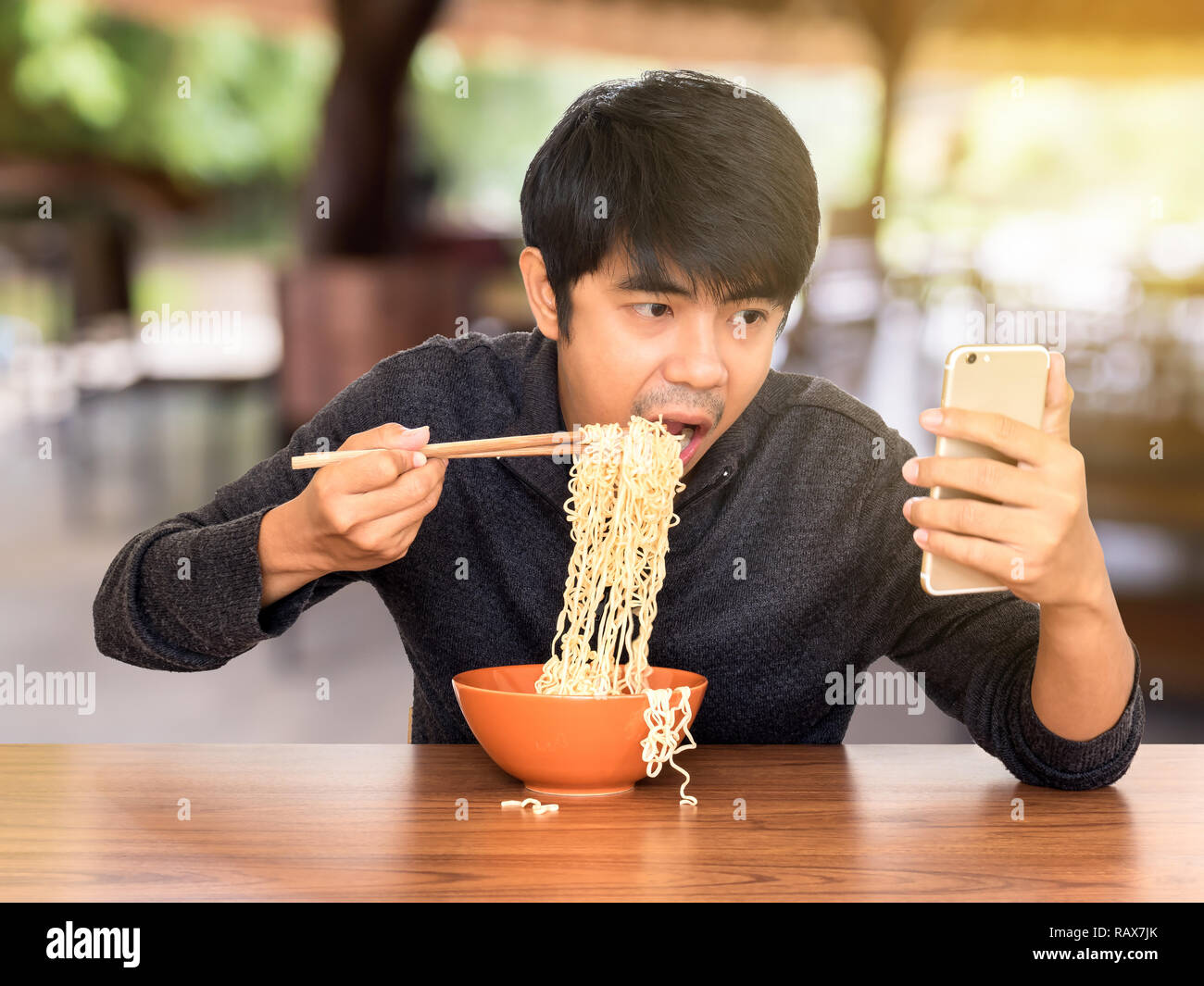 Mann essen chinesische Nudelsuppe monströs während der Suche und Verwendung von Smartphones. Konzept der Smartphone sucht, phubbing oder soziales Netzwerk Probleme Stockfoto