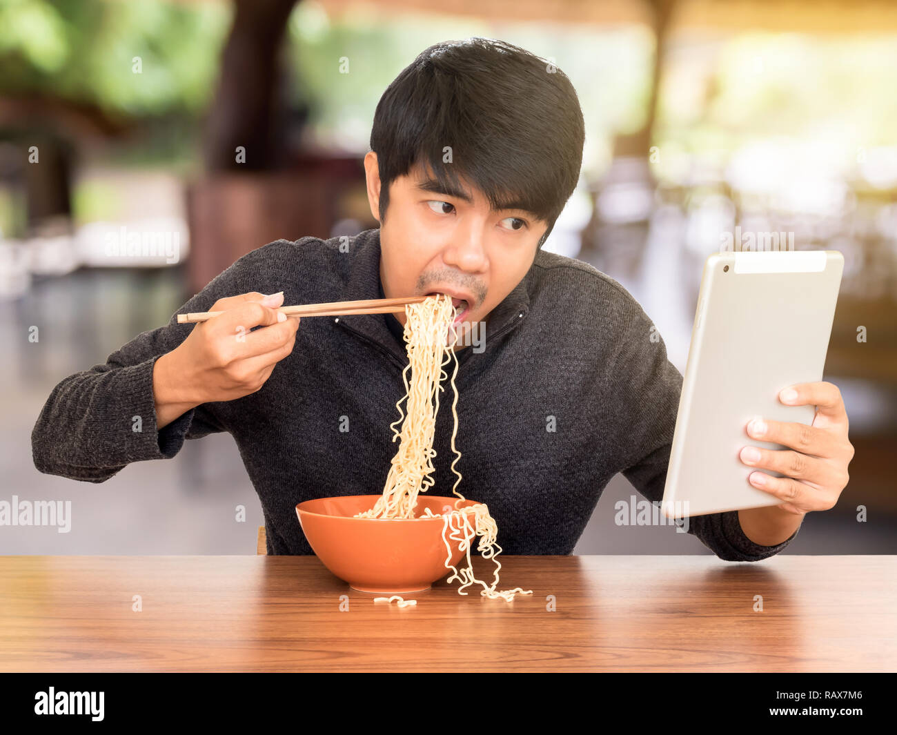 Mann essen chinesische Nudelsuppe monströs während der Suche und Verwendung von Tablet. Konzept der Smartphone sucht, phubbing oder soziales Netzwerk Probleme Stockfoto