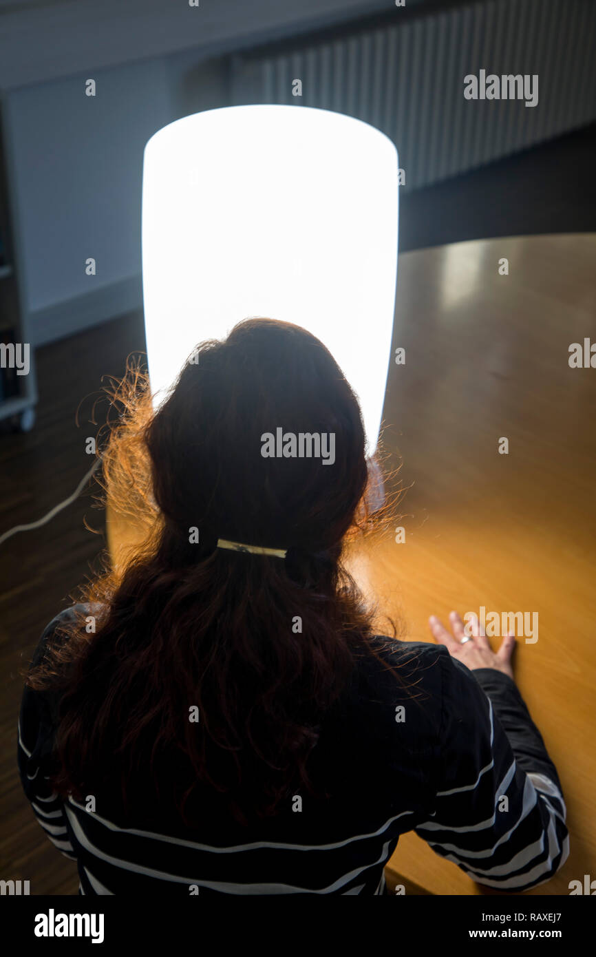 Die Lichttherapie mit Tageslicht Lampe, eine Frau sitzen vor eine Lampe, die Tageslicht imitiert, Therapie gegen Winter Depression, weil zu wenig Stockfoto