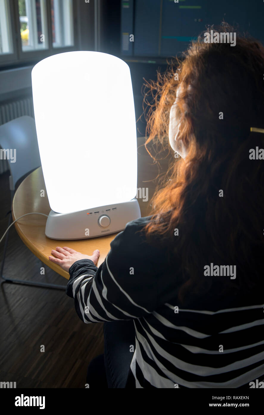 Die Lichttherapie mit Tageslicht Lampe, eine Frau sitzen vor eine Lampe, die Tageslicht imitiert, Therapie gegen Winter Depression, weil zu wenig Stockfoto