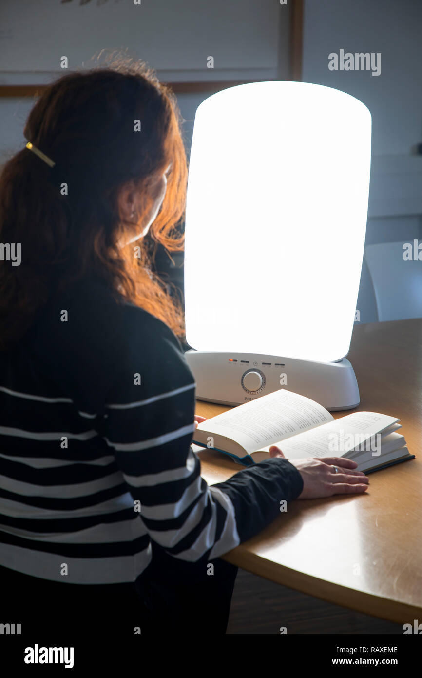 Lichttherapie mit Tageslichtleuchte, eine Frau sitzt vor einer Artikel Leuchte, sterben Tageslicht imitiert, Therapie gegen Winterdepression, wegen zu wenig Vorteile Stockfoto
