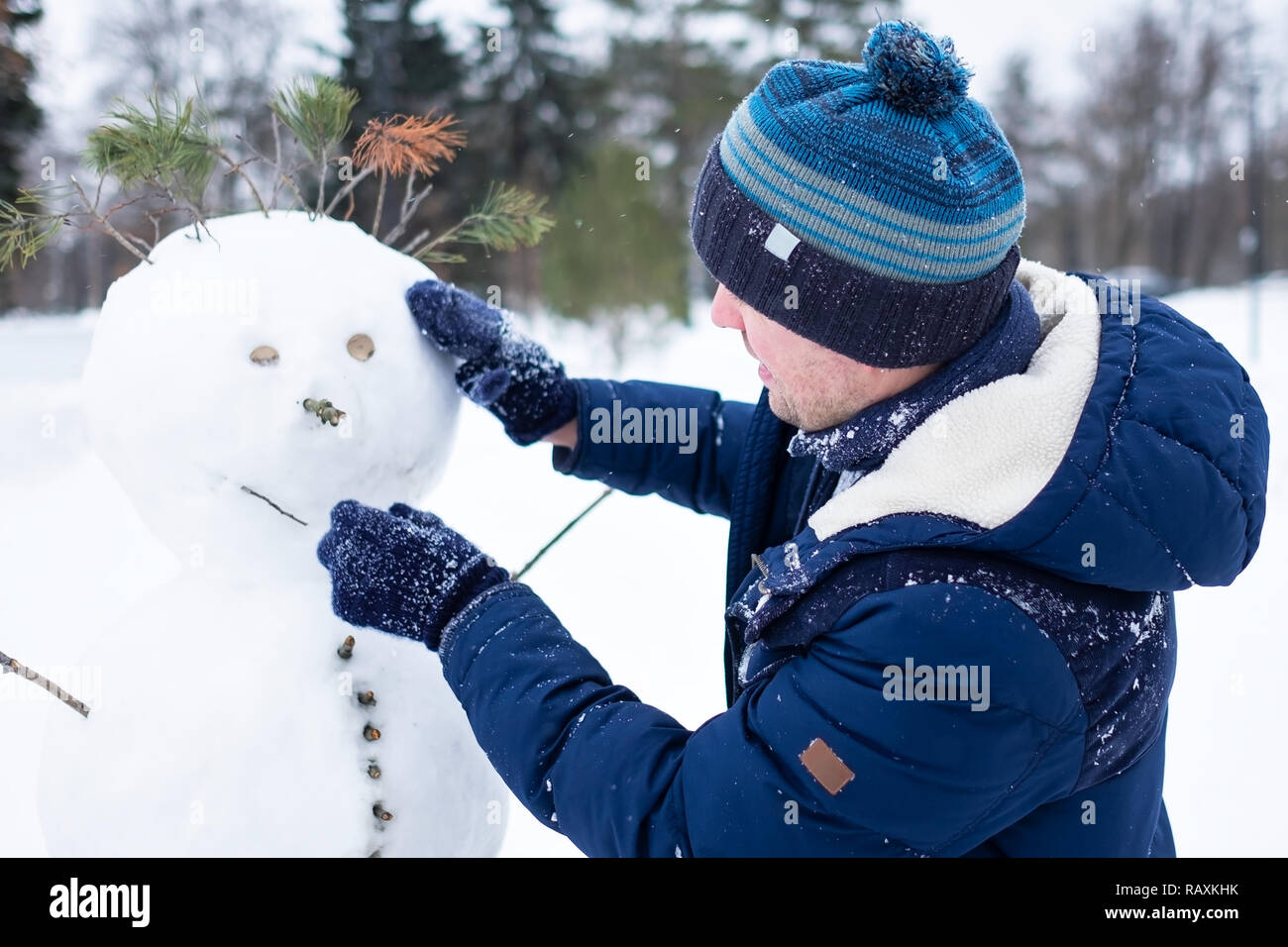 Junge europäische Mann in warme Kleidung, Schneemann aus Schnee outdoor. Spaß wie ein Kind im Winter Urlaub. Stockfoto