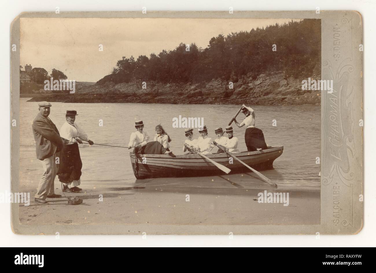 Frühe edwardianische Kabinettkarte von 7 jungen Damen und Mädchen mit langen Röcken und Strohboatern, die sich amüsieren und ein Ruderboot in Mill Bay, Salcombe, Devon, Großbritannien, im Sommer Juni 1901 landen Stockfoto