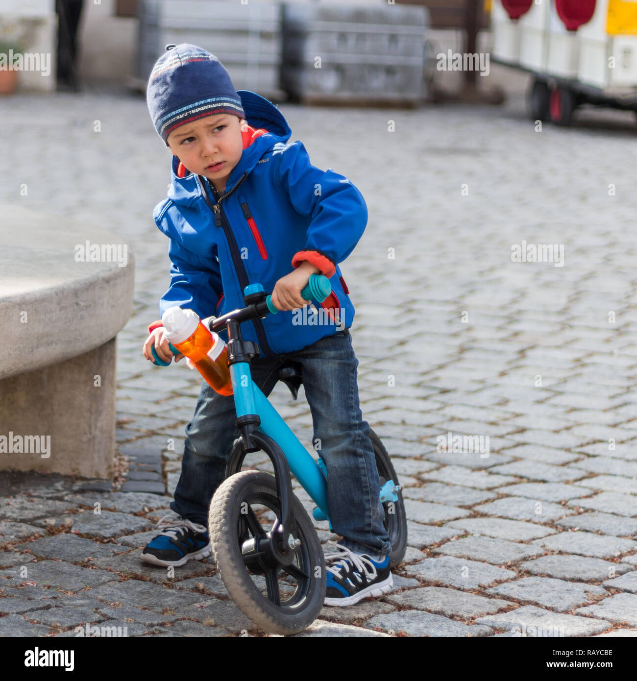 Kind Junge, das sein Fahrrad stoppt und wütend aussieht, trägt blauen Mantel und Kappe Stockfoto