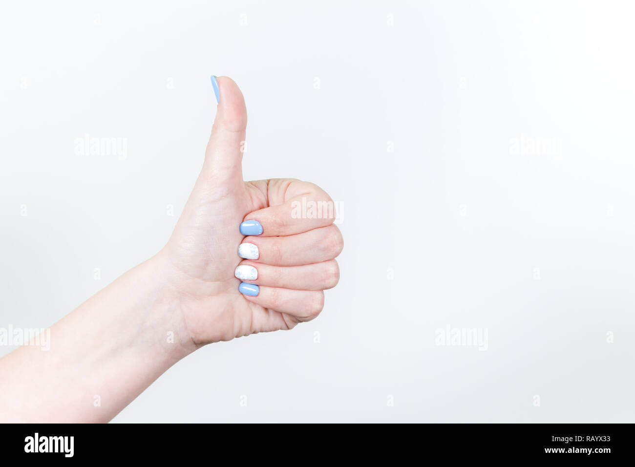 Detailansicht der weiblichen Jungen Hand in Gestalt Geste mit dem Daumen oben auf weißem Hintergrund. Fingernägel mit weißen und blauen professionellen modernen Stockfoto
