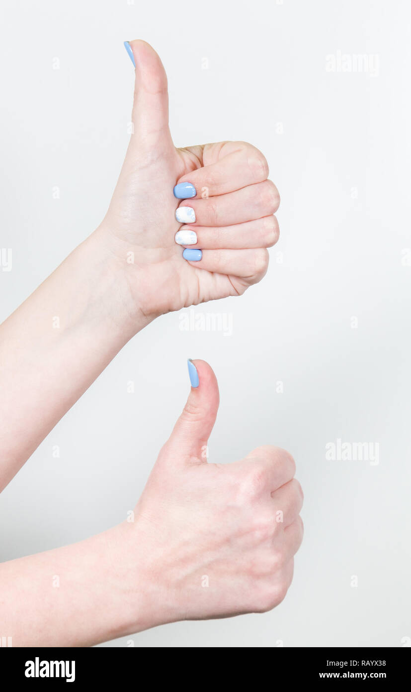 Detailansicht von zwei weiblichen Händen im Gleichnis Geste mit dem Daumen oben auf weißem Hintergrund. Fingernägel mit weißen und blauen professionellen modernen g Stockfoto