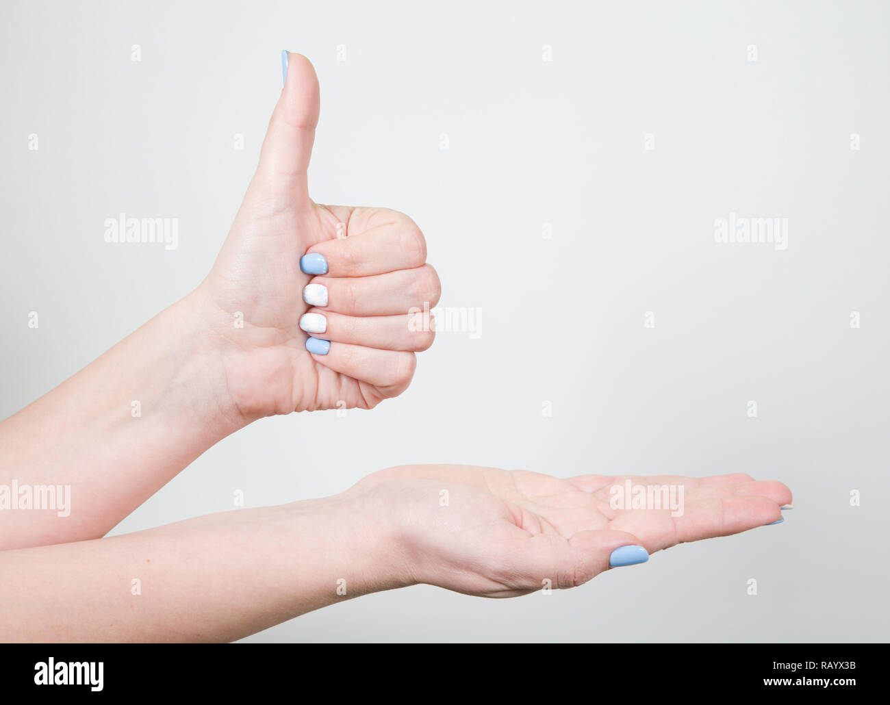 Detailansicht der weiblichen Jungen Hand in Gestalt Geste mit dem Daumen oben auf weißem Hintergrund. Fingernägel mit weißen und blauen professionellen modernen Stockfoto