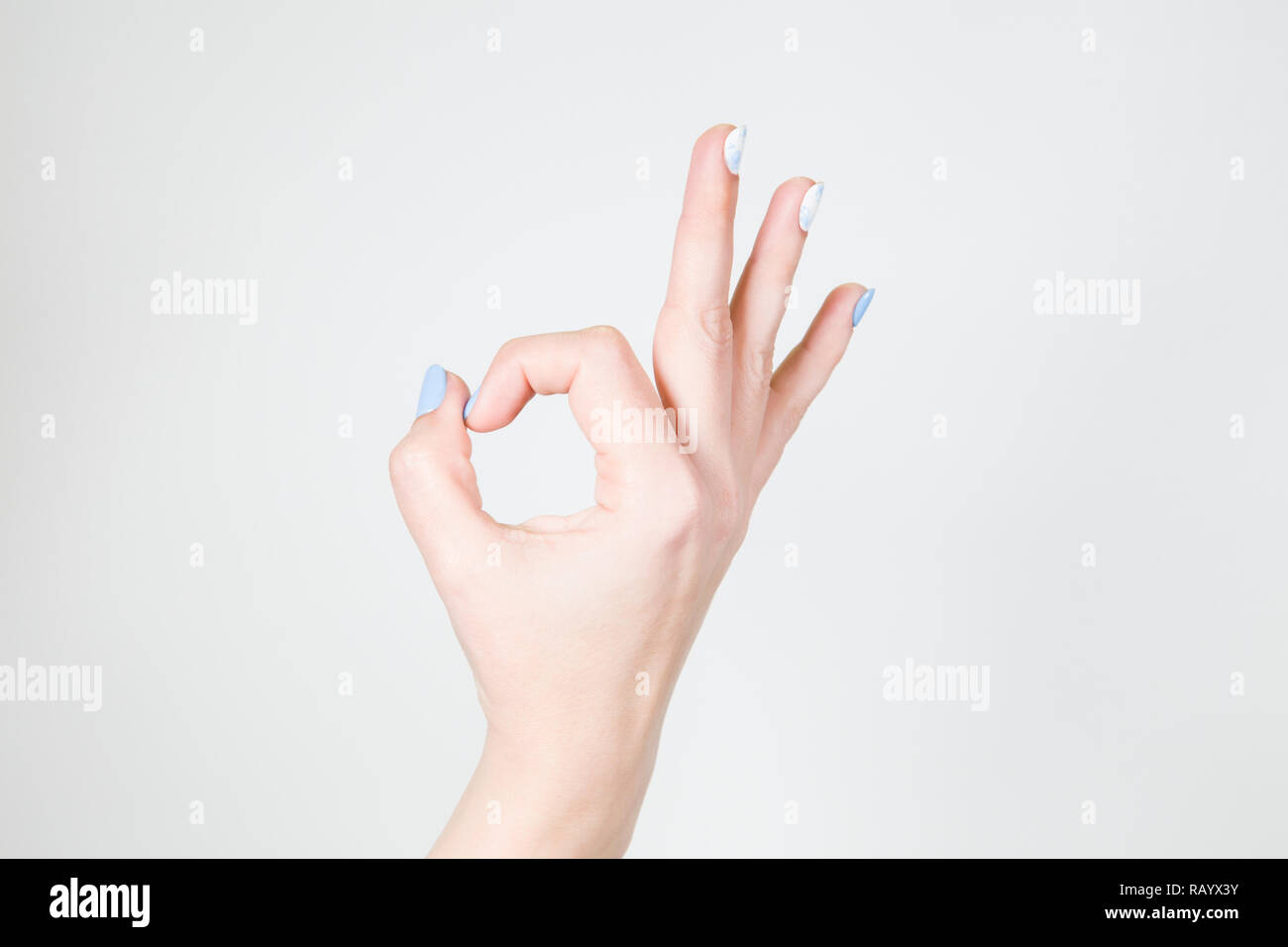 Detailansicht der Weißen weiblichen Hand in Ordnung Geste auf weißem Hintergrund. Fingernägel mit modernen Gel polish Maniküre aus weißen und blauen Farben. Stockfoto