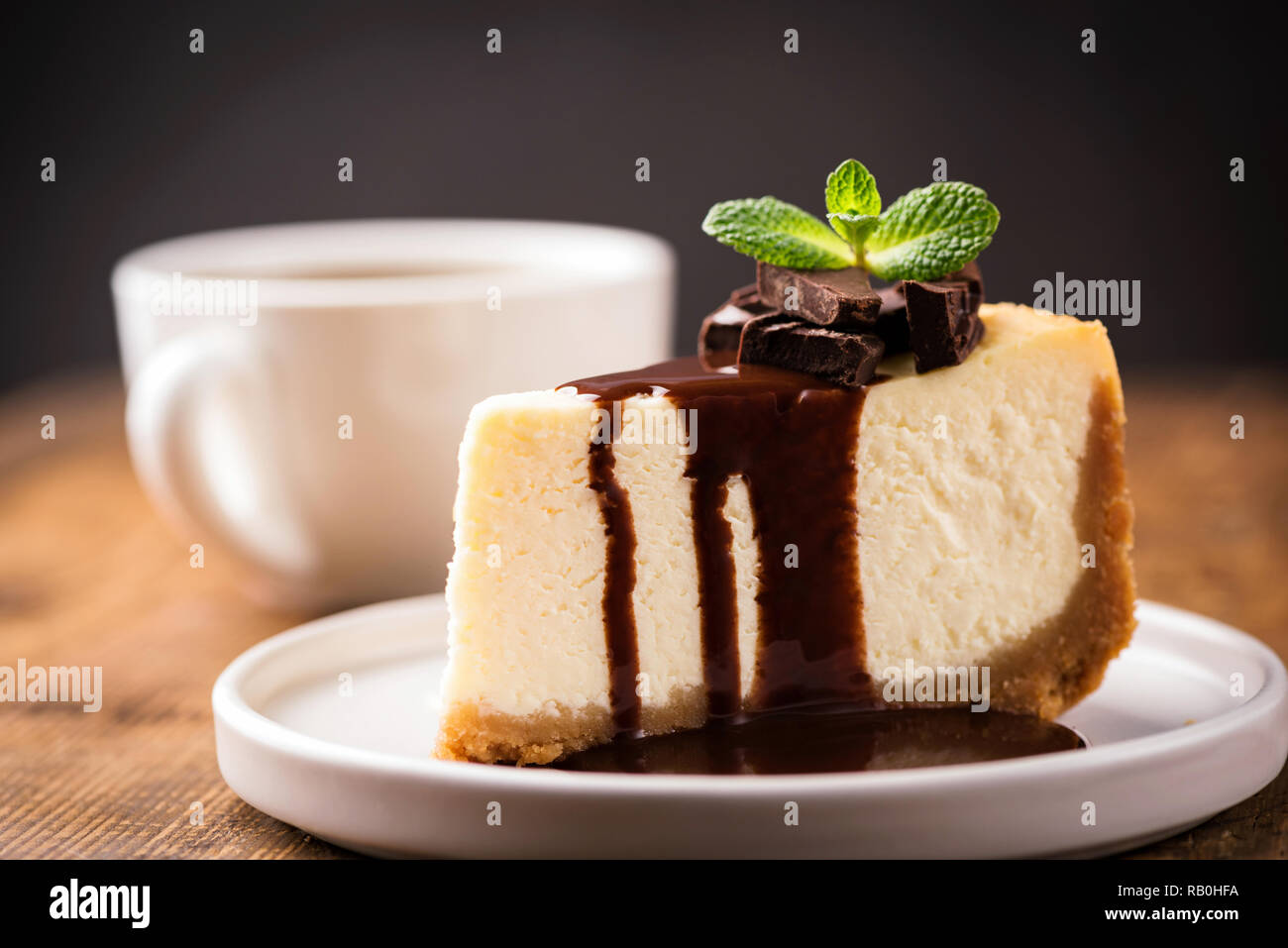 Käsekuchen mit Schokoladensauce und Tasse Kaffee. Scheibe des klassischen New York Cheesecake mit Schokoladensauce gegossen und mit minzeblatt eingerichtet Stockfoto