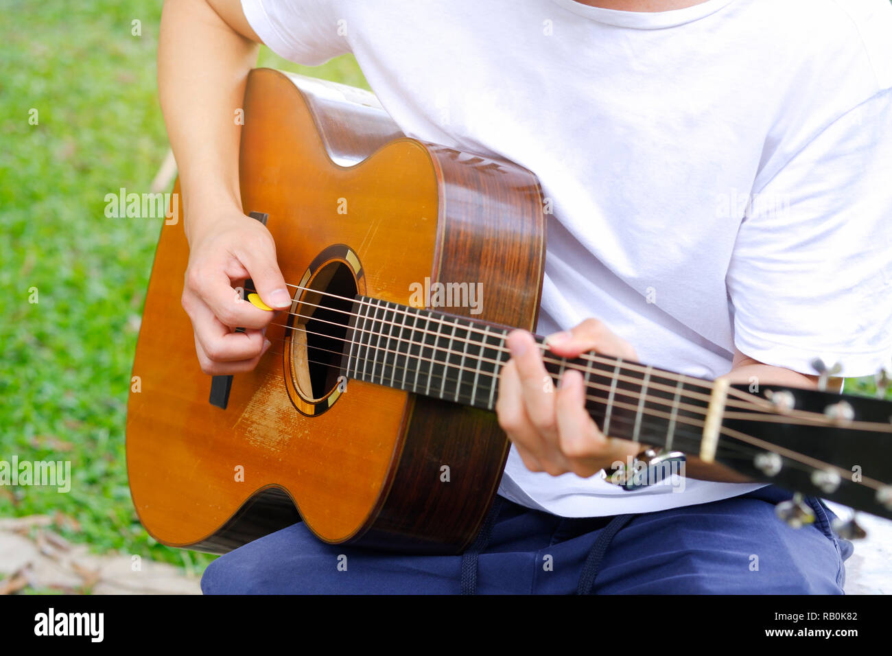 Junge Mann spielt akustische Gitarre im Garten Stockfoto