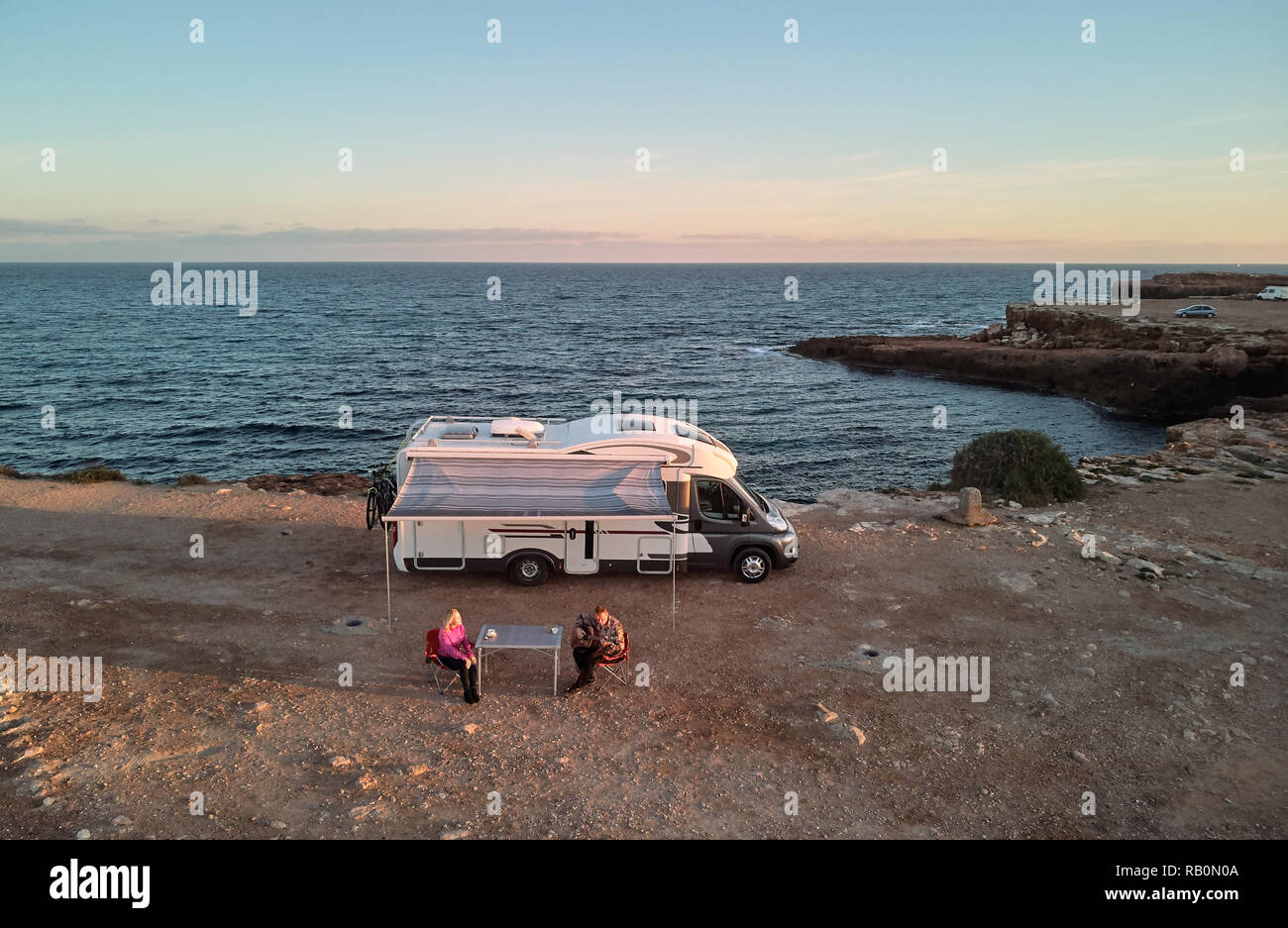 Antenne oben anzeigen Paar mittleren Alters sitzen auf Klappstühlen in der Nähe von recreational vehicle Camper Trailer an der felsigen Küste des Mittelmeers. Husb Stockfoto
