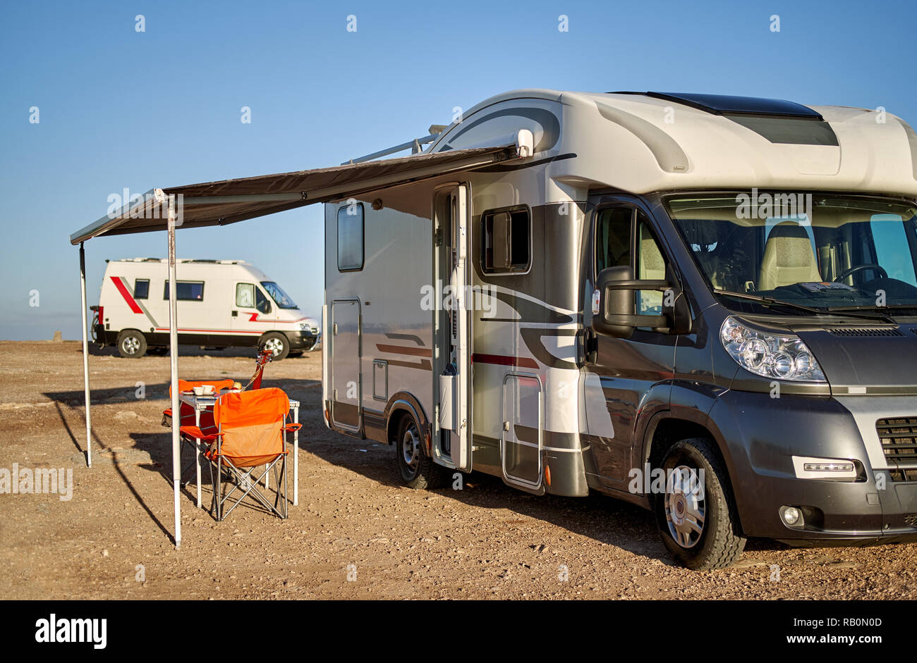 Leere faltbare Stühle und Tisch unter dem Vordach in der Nähe von neuen modernen recreational vehicle Camper Trailer. Abenteuer, aktive Menschen reisen mit Motor home Conc Stockfoto