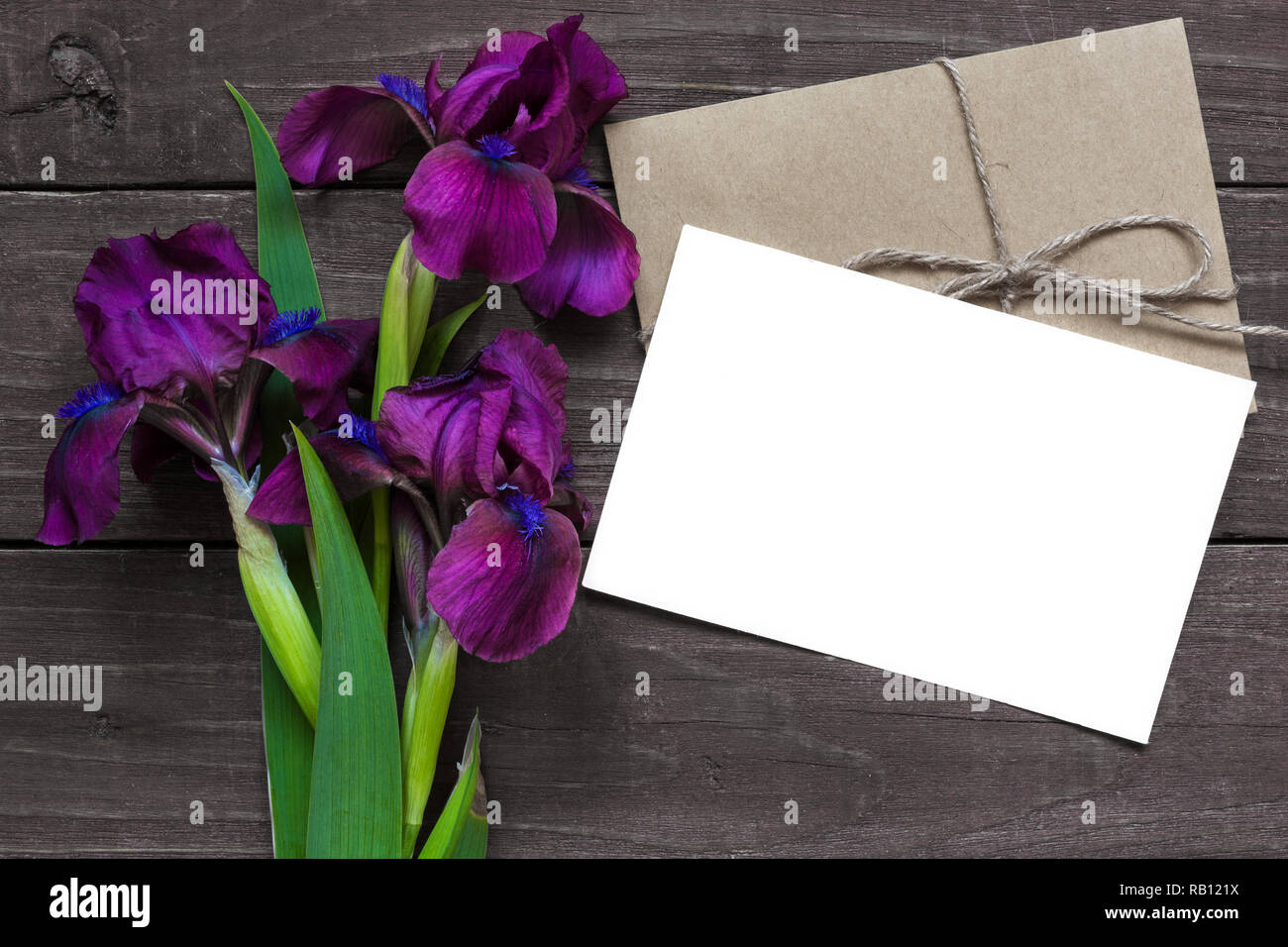 Leere weiße Gruß Karte und Umschlag mit lila iris Blumen mockup auf dunklen rustikalen, mit Holz Hintergrund für kreative Arbeit Design. top anzeigen. Flach Stockfoto