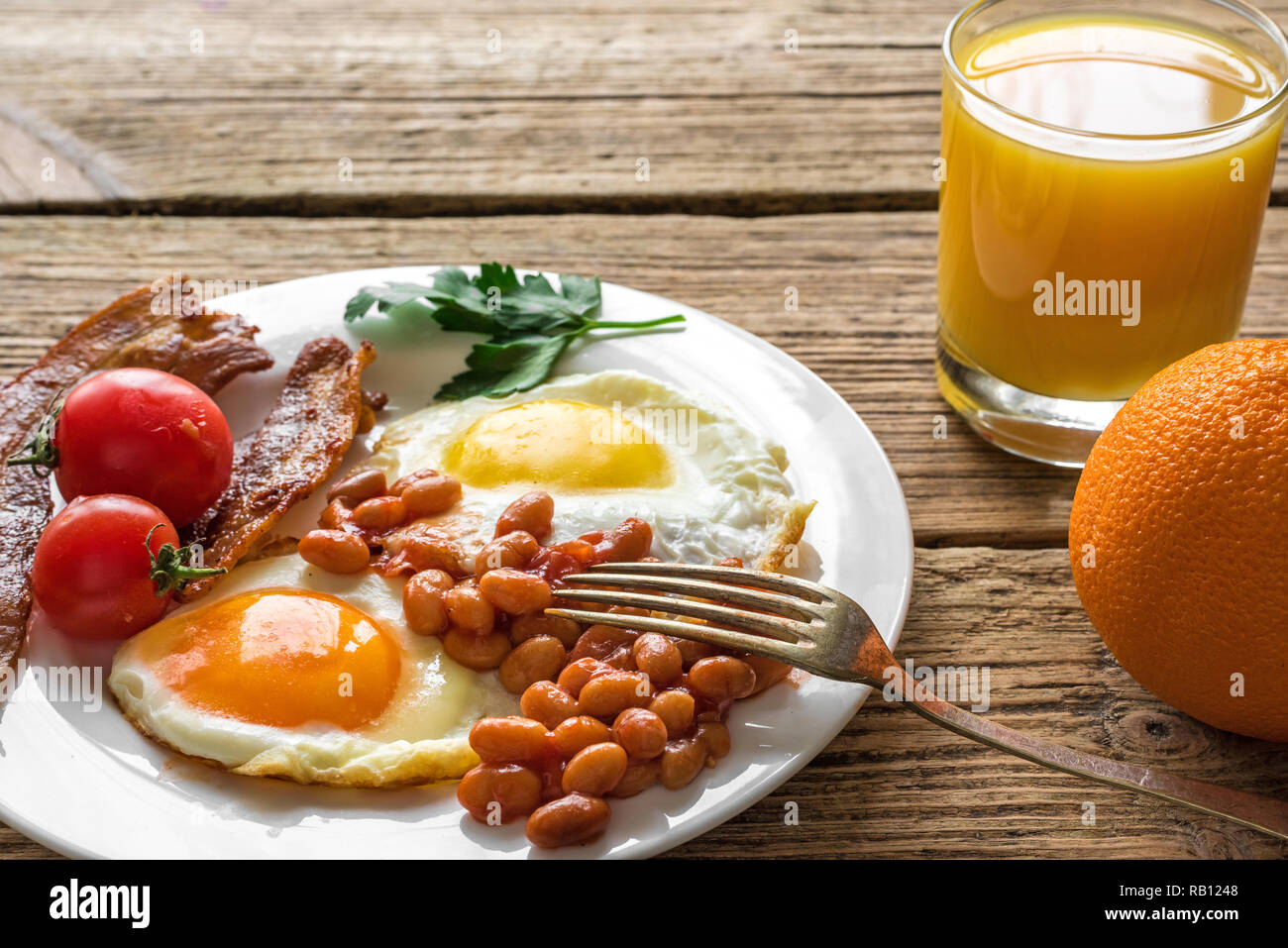 Englisches Frühstück serviert auf einem Teller mit Spiegelei, Bohnen, Tomaten und Speck mit frischem Orangensaft auf hölzernen Tisch. Nach oben Schließen Stockfoto