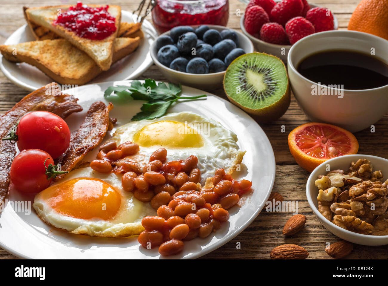 Englisches Frühstück. Spiegelei, Bohnen, Tomaten, Kaffee, Speck und Toast mit Nüssen, frischen Früchten und Beeren. Nach oben Schließen Stockfoto