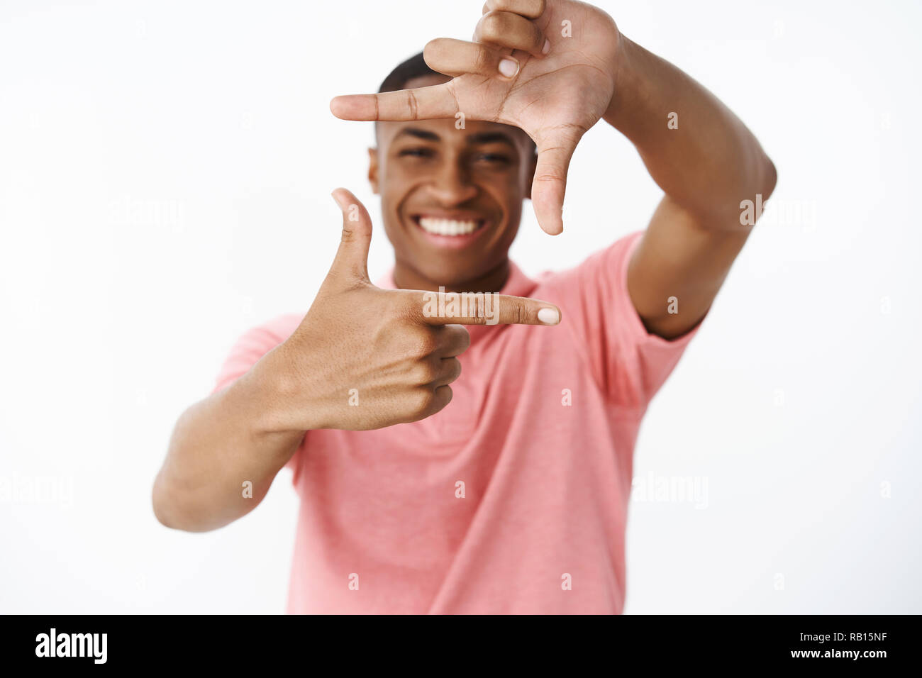 Kerl will merken Freundin Lächeln, Hände, Rahmen mit Fingern und lächelnd durch es genießen, Träumen über Zukunft und Planung wie Design neue Wohnung über grauer Hintergrund Stockfoto