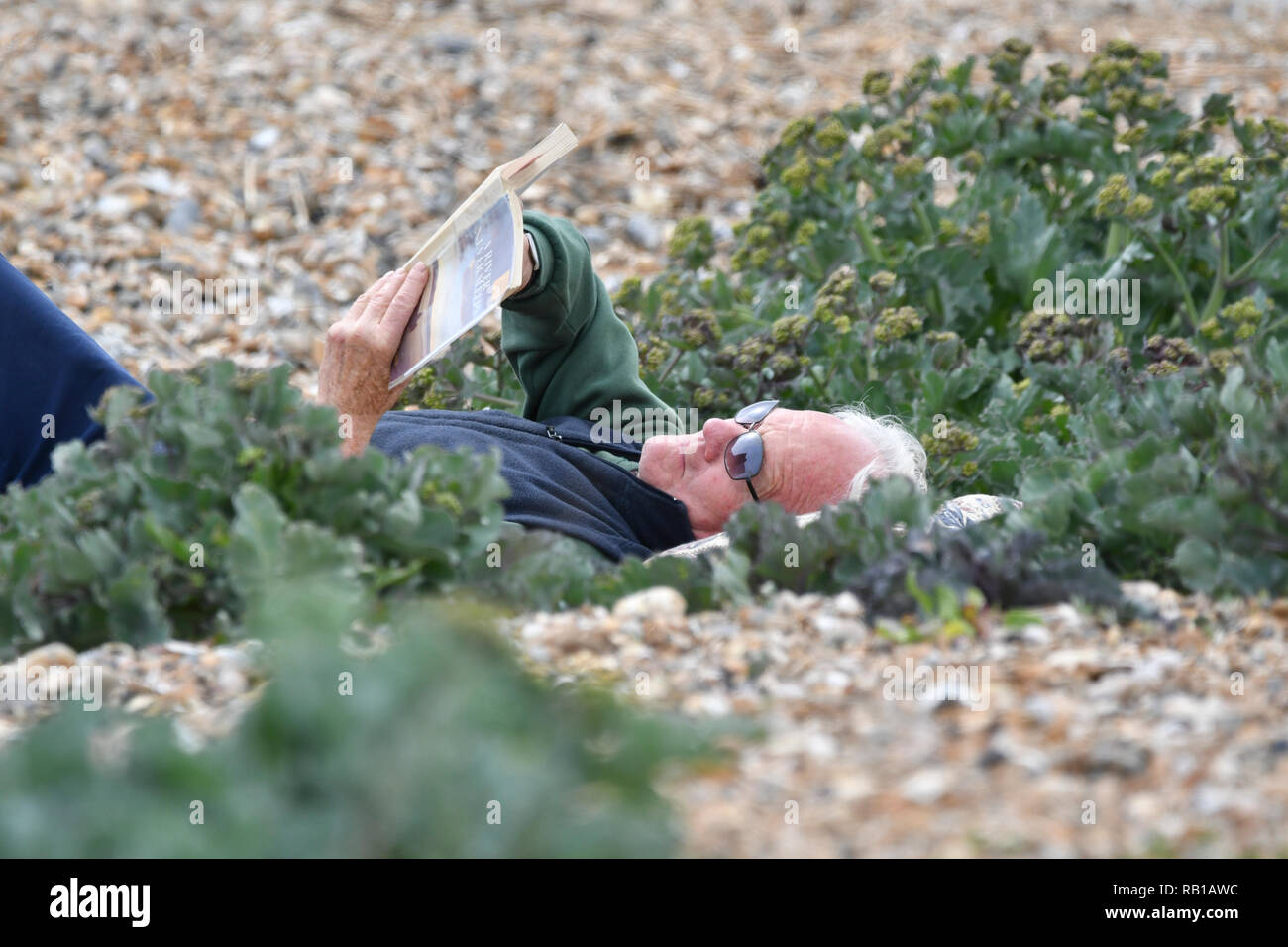 Ein Mann auf dem Rücken am Strand ein Buch lesen an einem kalten Tag im Frühling, in Großbritannien. Stockfoto