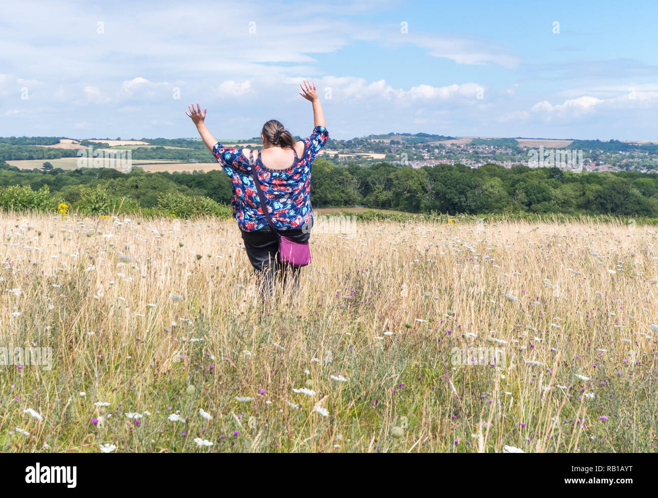 Junge Frau vor Freude hüpfend auf einer Wiese in der Britischen Landschaft, UK. Laufen und springen. Happy Konzept. Arme nach oben. Das Springen in einem Feld. Stockfoto