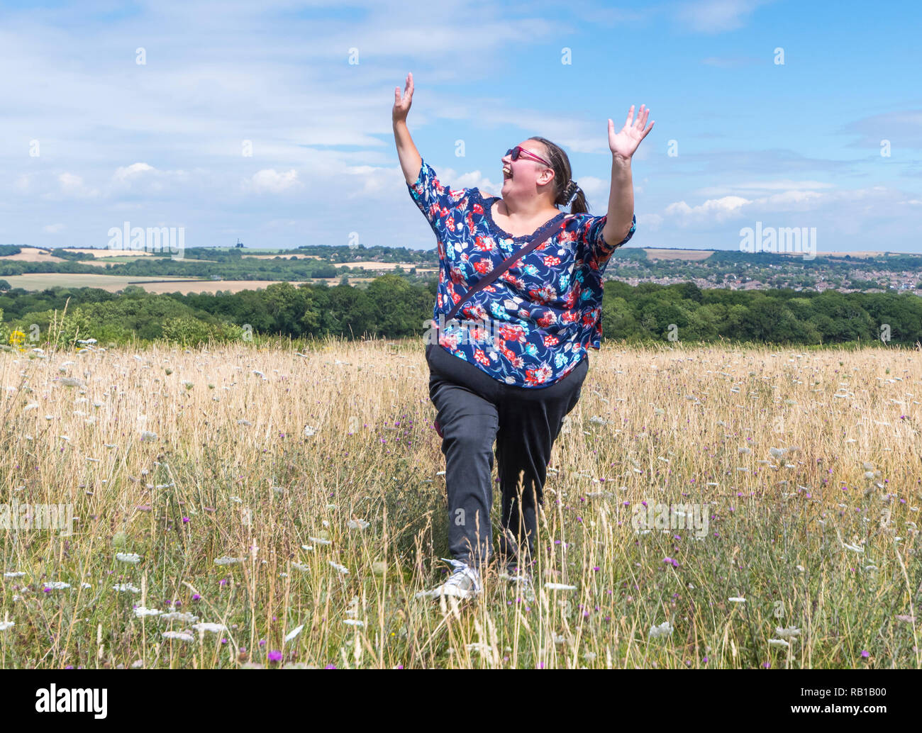 Junge Frau vor Freude hüpfend auf einer Wiese oder einem Feld in der Landschaft, UK. Laufen und springen. Happy Konzept. Arme nach oben. Glück Konzept. Stockfoto