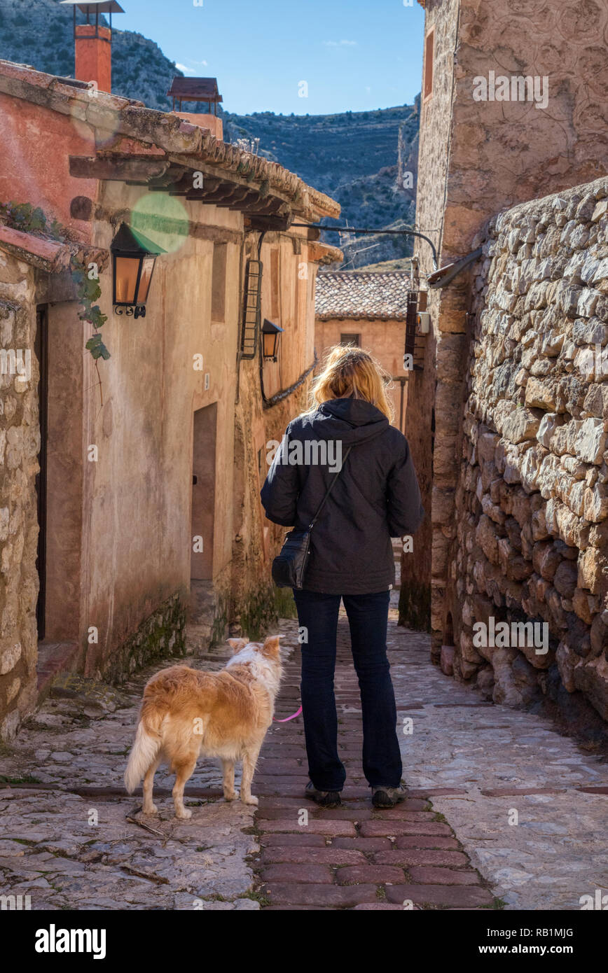 Eine blonde Frau, die eine zufällige Kopfsteinpflaster Spanisch Straße in der kleinen Stadt Albarracin mit ihrem blonden Border Collie mix Hund und einem Hauch von Su Stockfoto