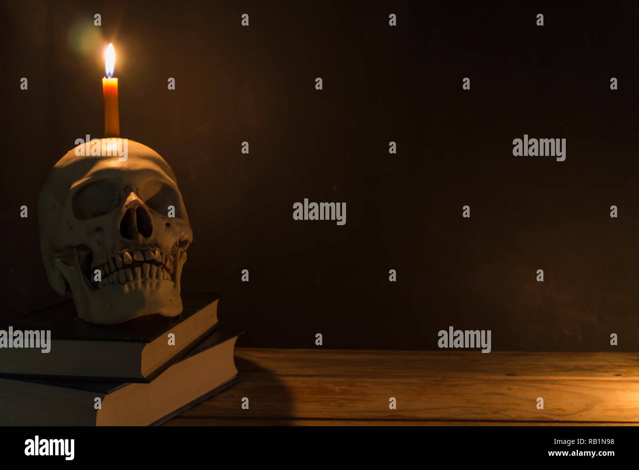 Menschlicher Schädel mit Kerzenlicht und das Buch auf dem Holztisch in den dunklen Hintergrund, Dekorieren für Halloween Theme mit kopieren. Stockfoto