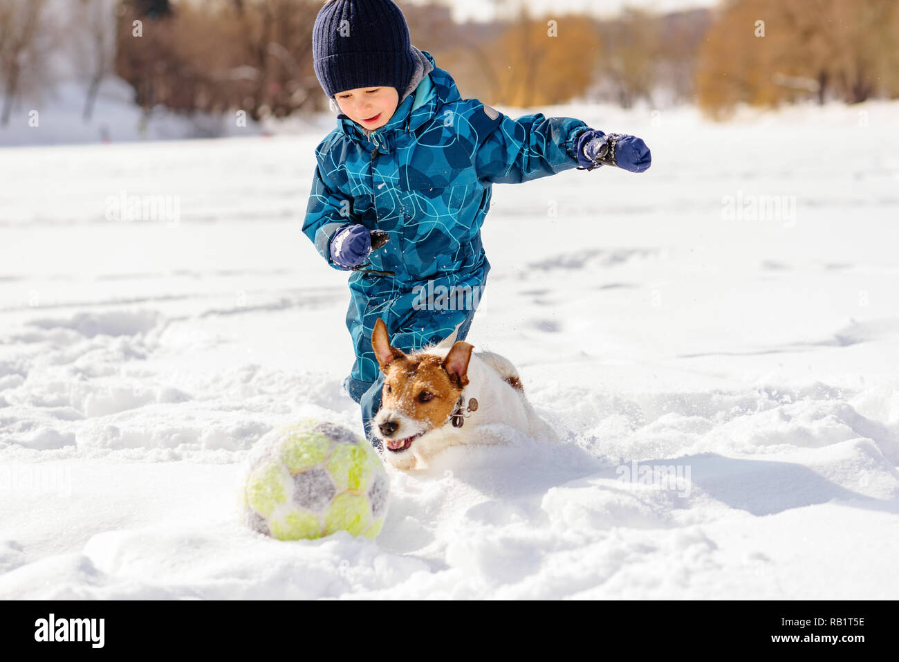 4 Jahre Junge spielt Fußball (Fußball) mit seinem Hund im Schnee Stockfoto