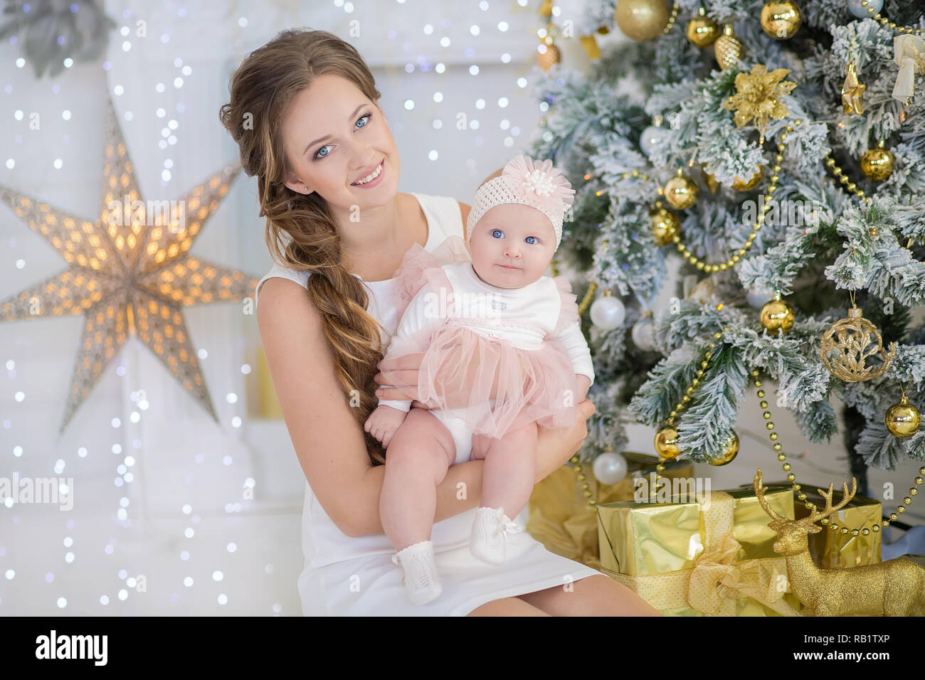 Mutter mit ein wenig Süßes und schöne Tochter verbringt Zeit spielt, coos, sitzen neben dem Weihnachtsbaum. Stockfoto