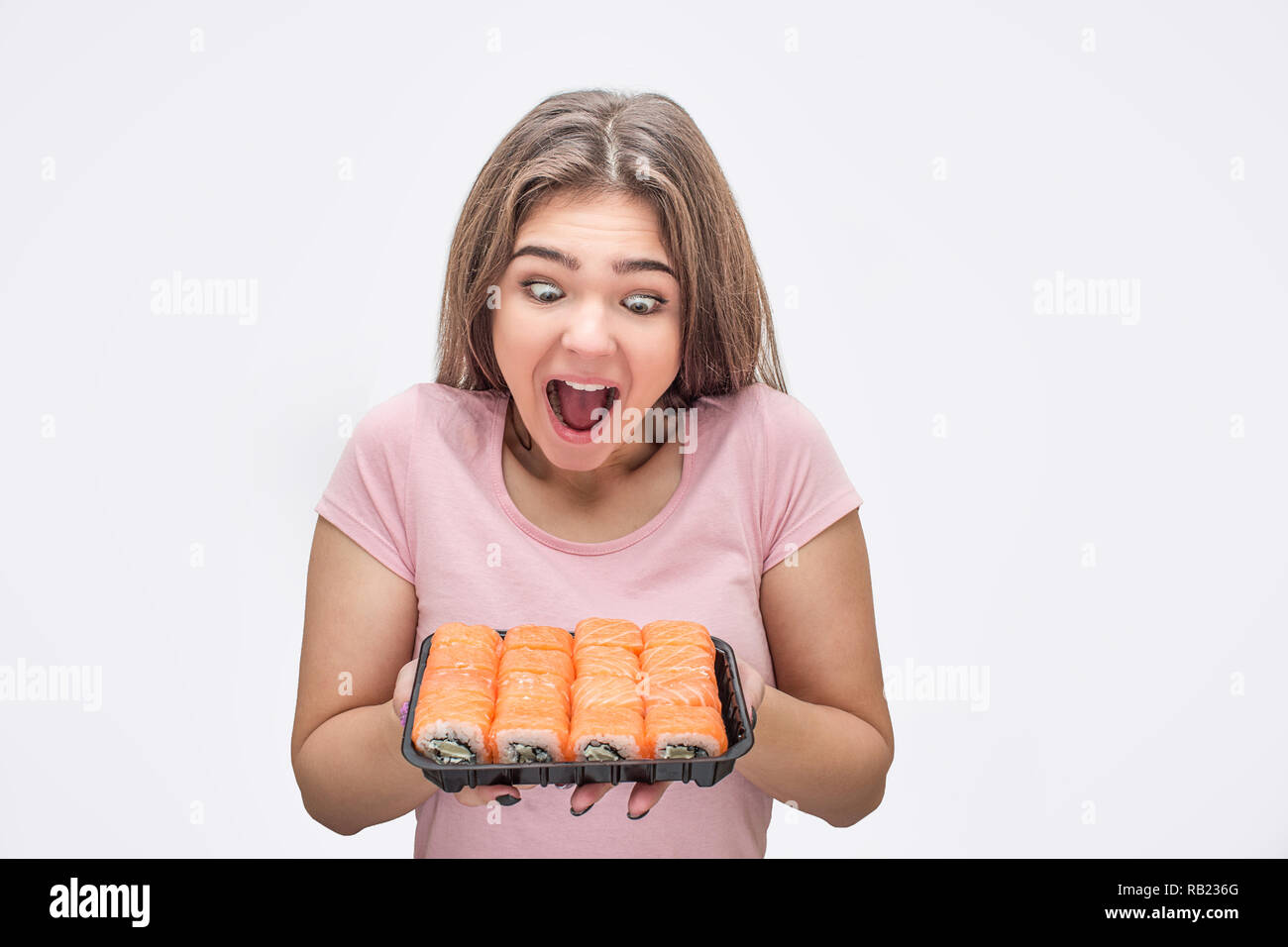 Junge Frau Blick auf Satz von frischem Sushi aufgeregt. Sie halten es in den Händen. Auf grauem Hintergrund. Stockfoto