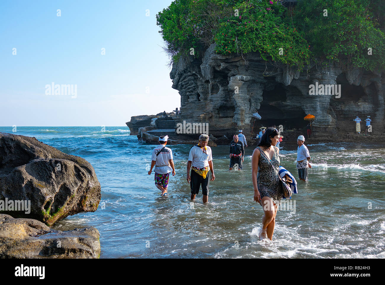 Bali, Indonesien - März 24, 2017: die Menschen das Meer auf die kleine Insel mit der Heiligen Höhle des Tanah Lot Tempel auf dem Meer zu gehen Stockfoto