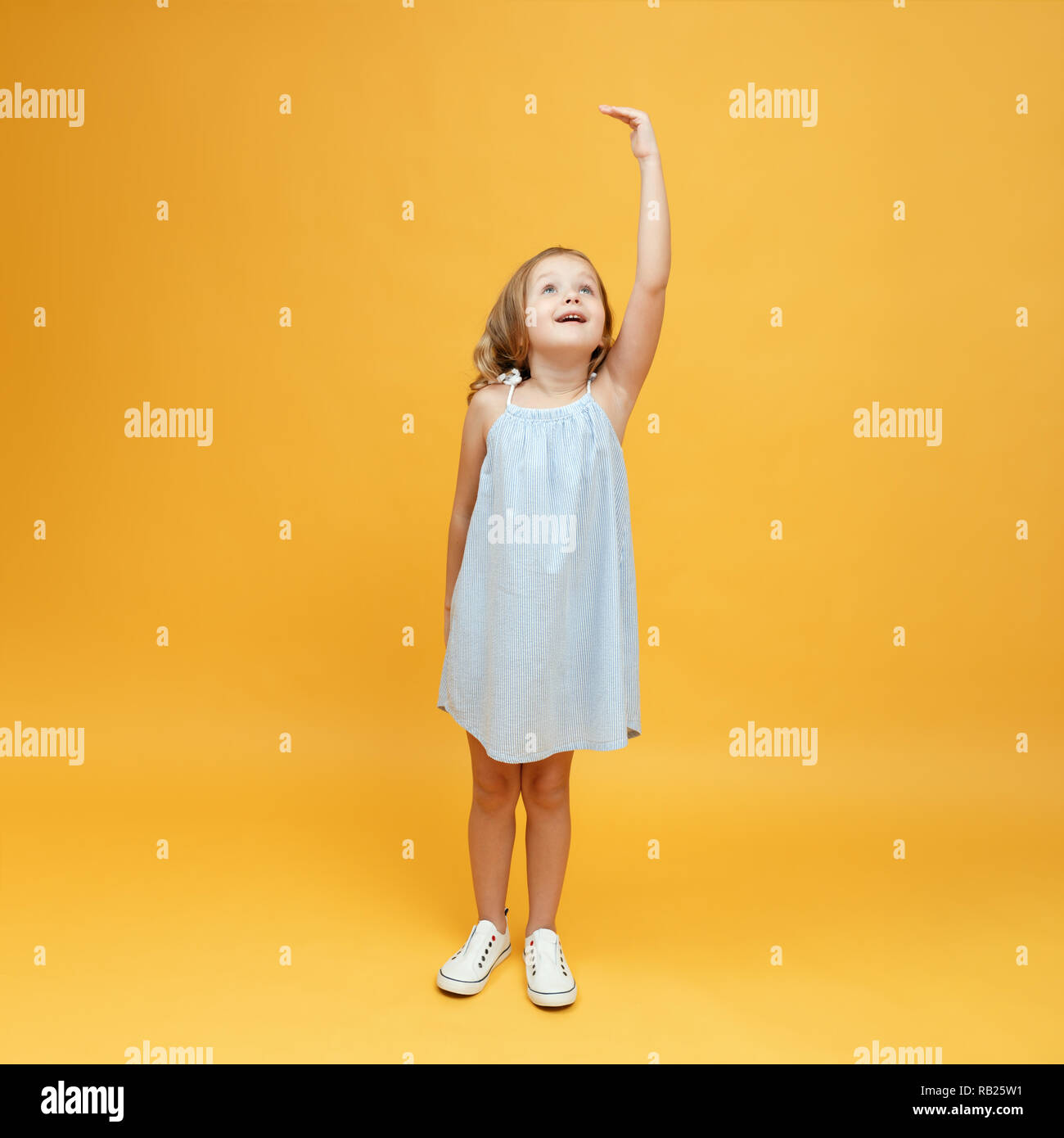 Ein kleines Kind Maßnahmen ihre Höhe auf einem gelben Hintergrund. Konzept der Entwicklung, Ziel, Erfolg Stockfoto