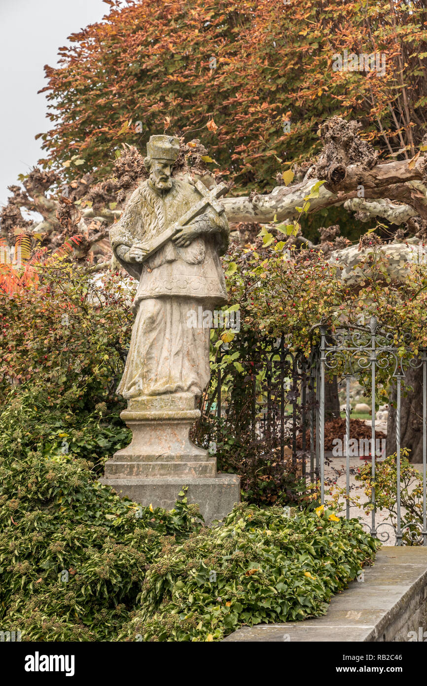 Steinerne Statue mit farbigen Blätter eines Baumes und Efeu Stockfoto