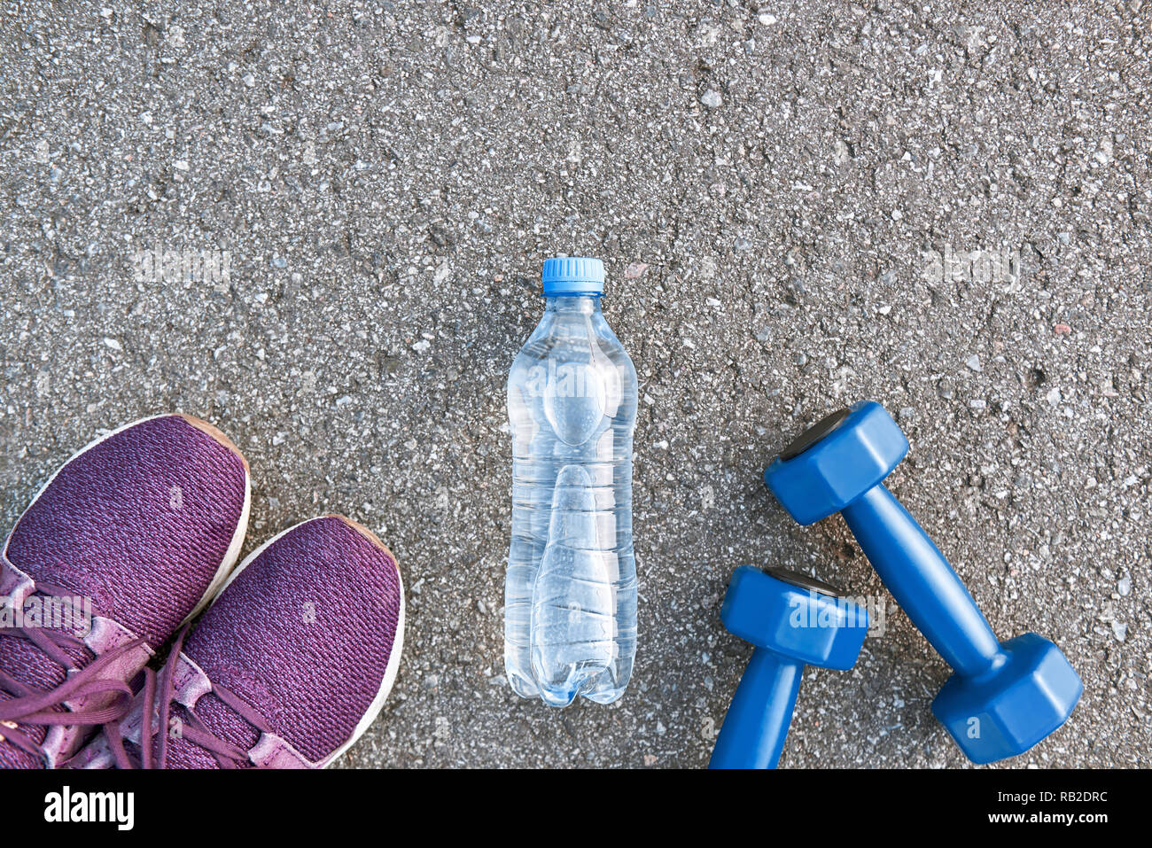 Motiviert zum Training. Zwei blaue dumpbells und eine Flasche Wasser liegen in der Nähe von Purple Sport Schuhe Stockfoto