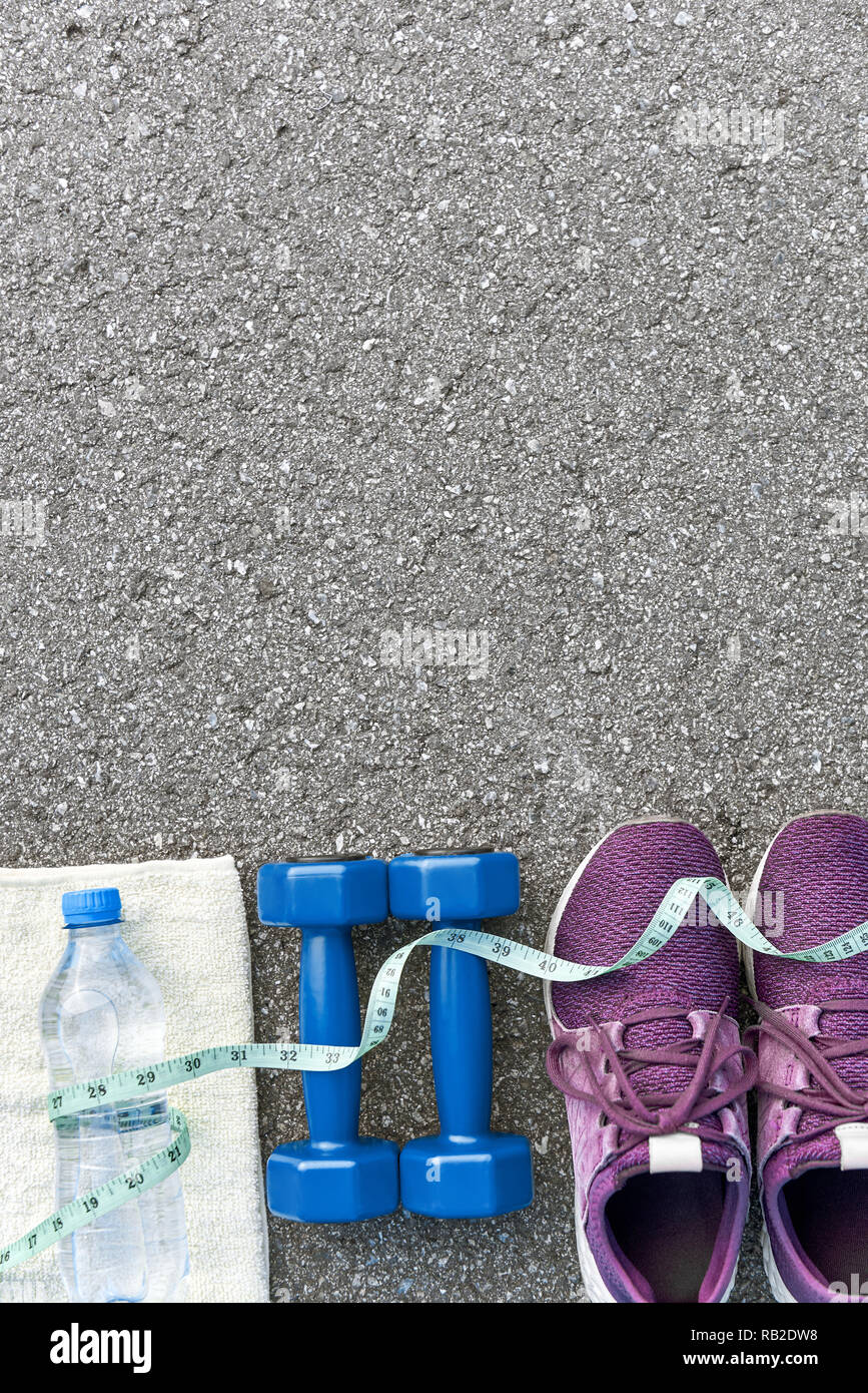 Motiviert zum Training. Zwei blaue dumpbells und eine Flasche Wasser liegen in der Nähe von Purple Sport Schuhe. Flasche, das auf weißem Handtuch, Maßband Abdeckungen Stockfoto